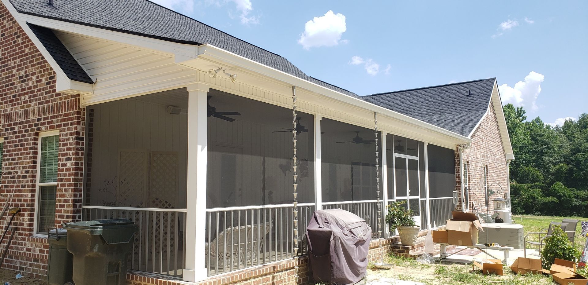 Screened porch with brick house, white trim, and a black roof on a sunny day.