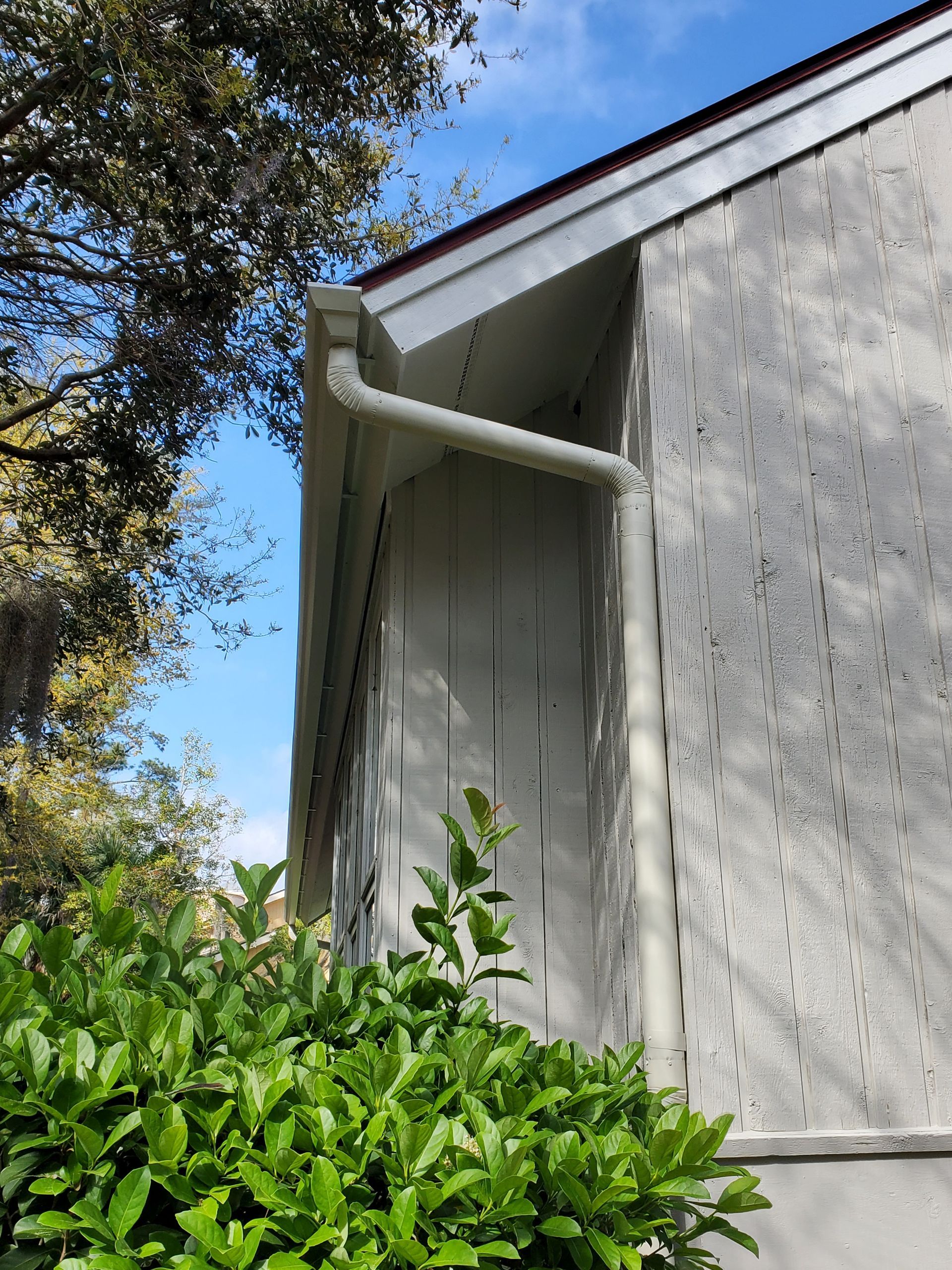 White gutters on a stucco building with a green bush and blue sky.