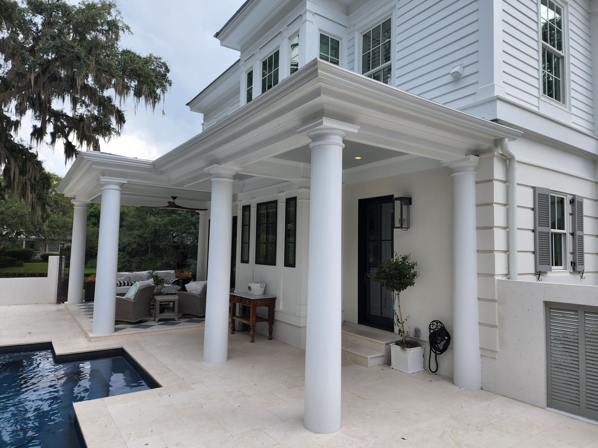 White house exterior with covered porch, columns, pool.