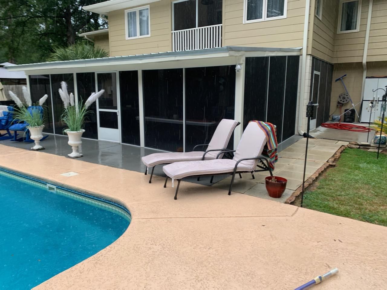 Poolside view: two lounge chairs on concrete patio next to a pool. Screened-in porch and beige house in background.