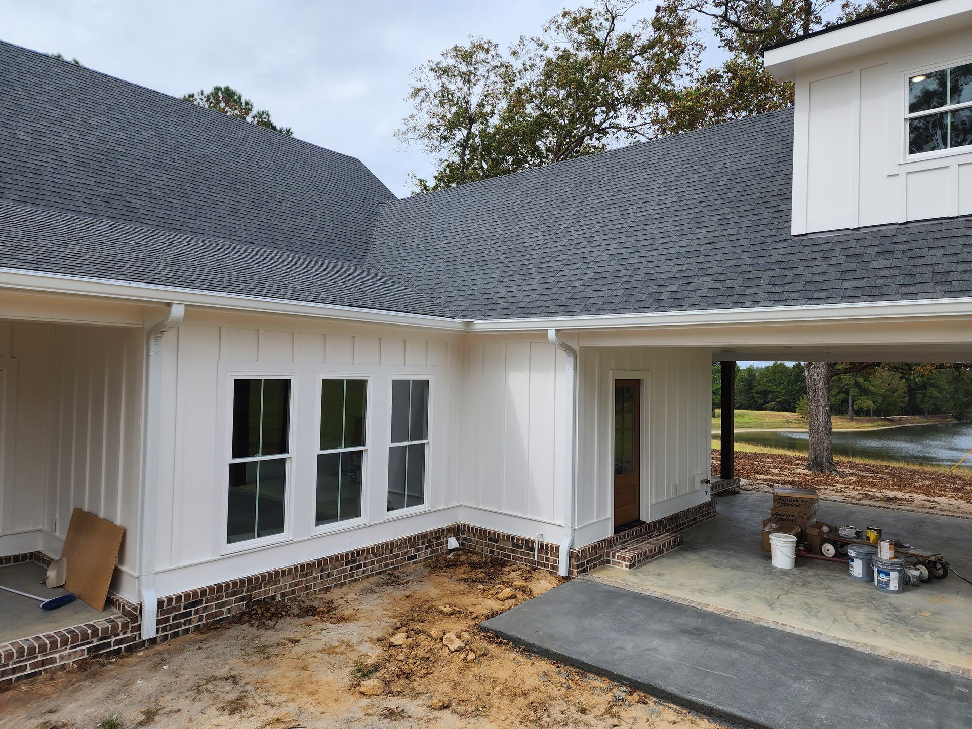 White house with dark gray roof, carport, and brick foundation. Construction materials visible.