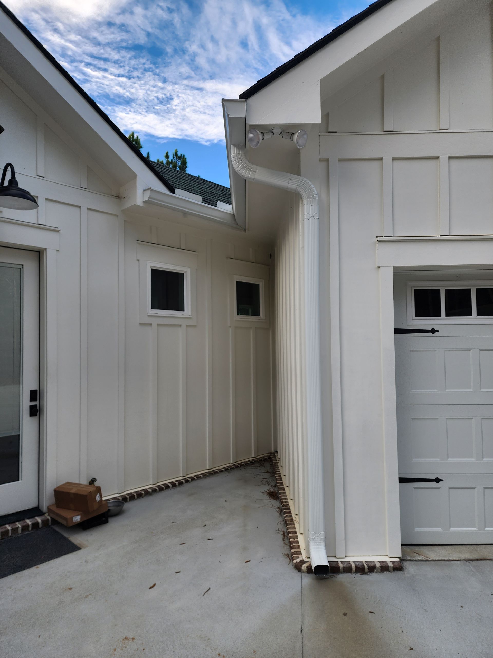 White house exterior with vertical siding, gutters, two small windows, and a garage door.