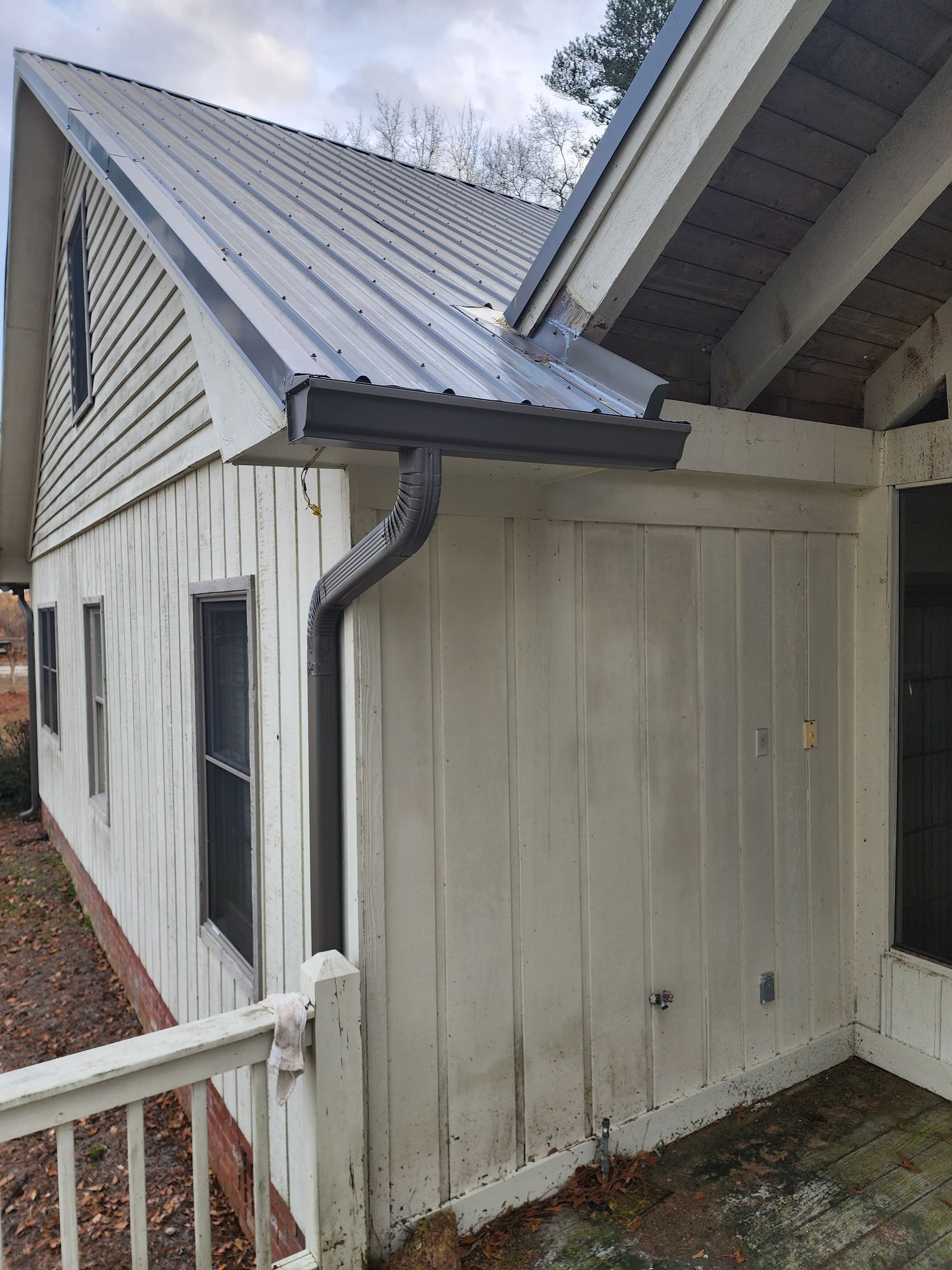 White building with gray metal roof, gutters. Side view, exterior shot.