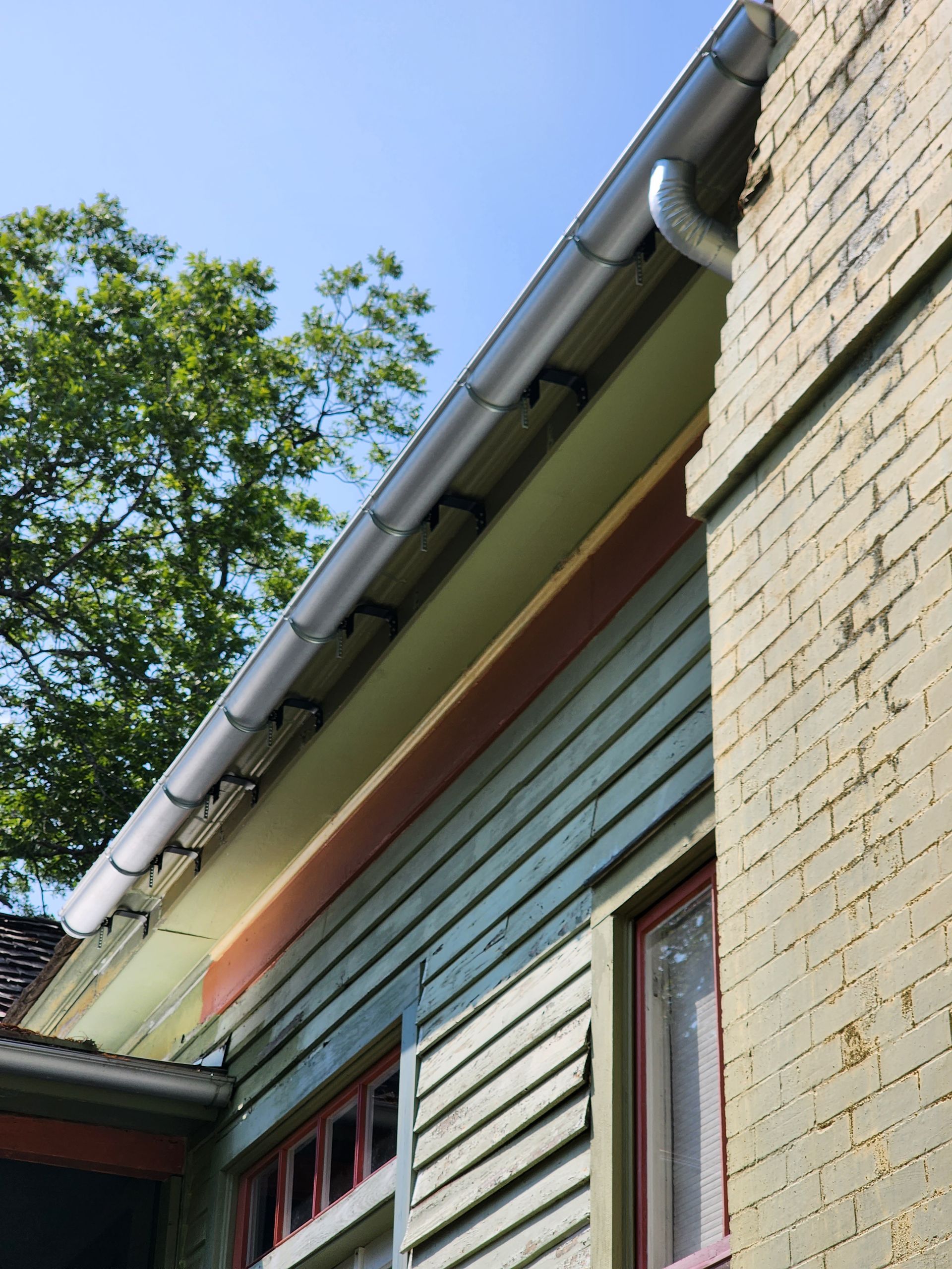 Gutter system along the edge of a light green house with gray brick wall, blue sky.
