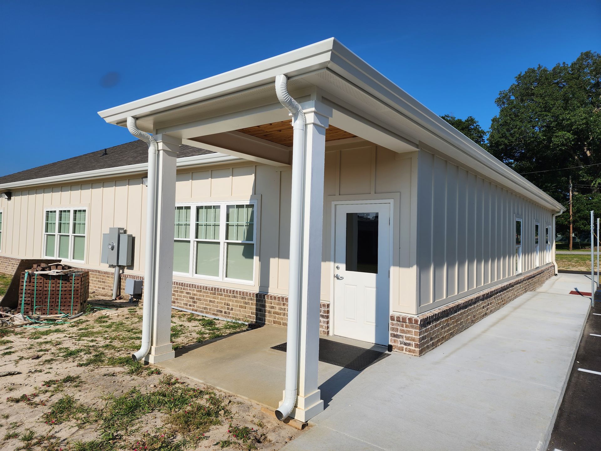 Cream-colored building with covered entrance, white columns, and brick base. Ramp leading to white door.