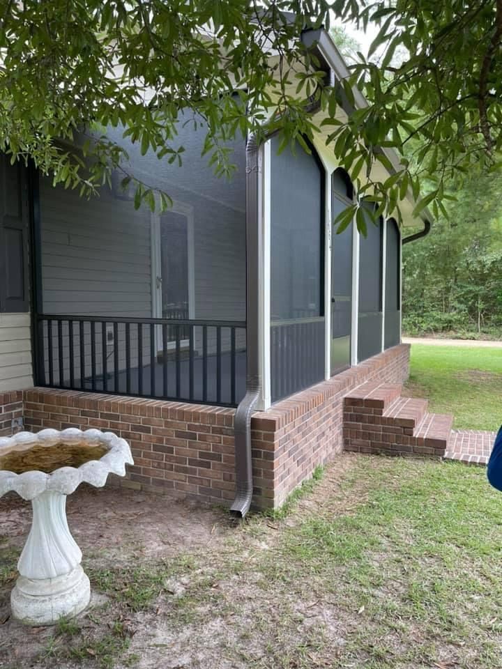 Screened porch with brick base and black railing. Birdbath in foreground.