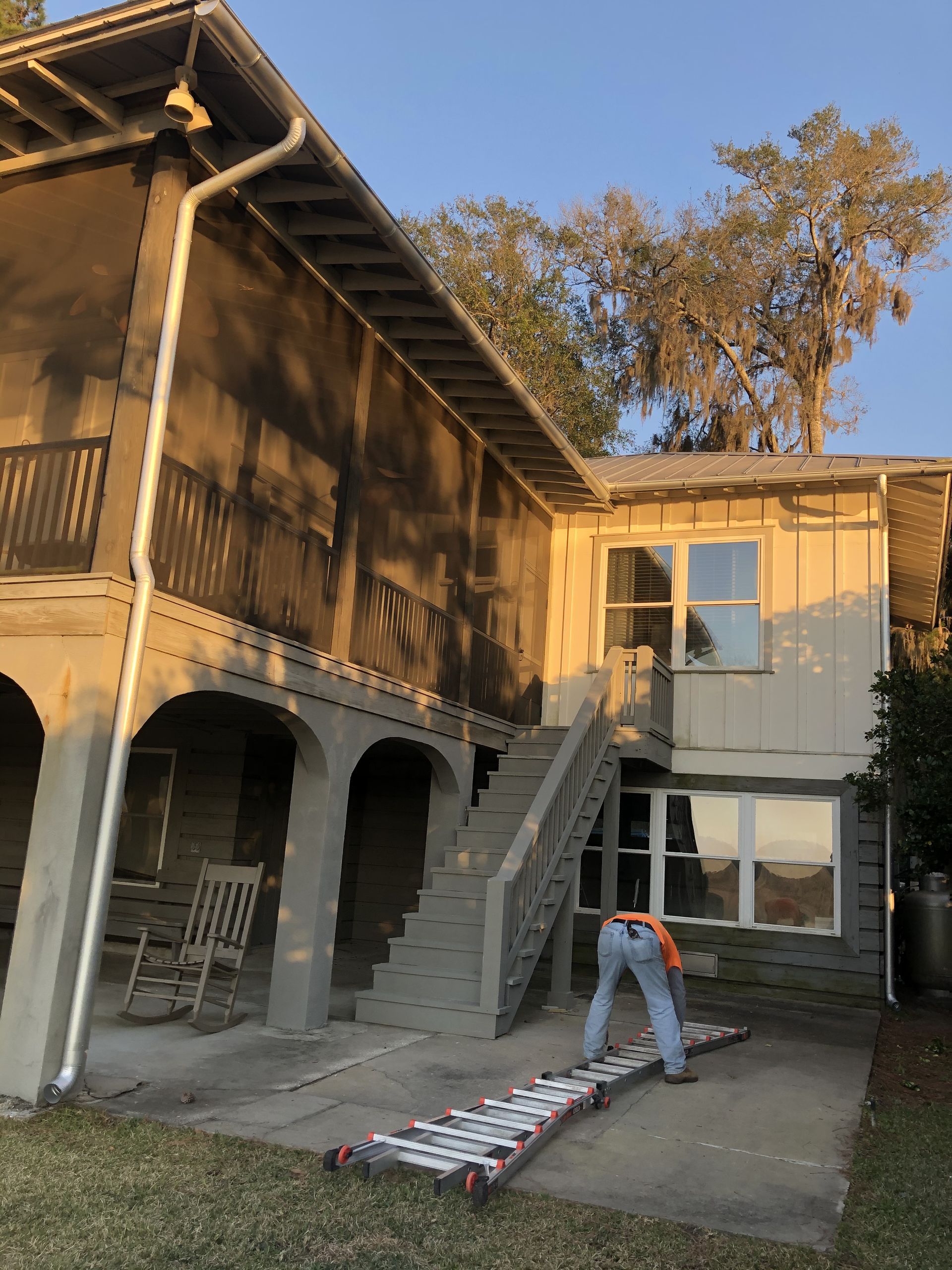A person on a ramp works near a two-story building with a screened porch and outdoor stairs.