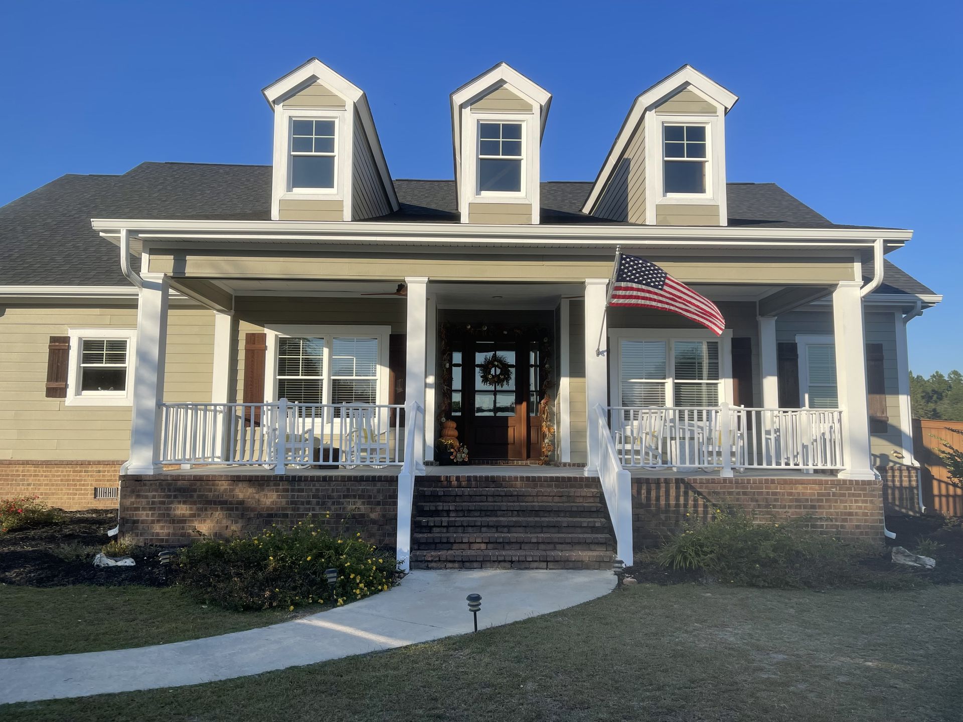 A two-story home with a porch and three dormers, American flag.