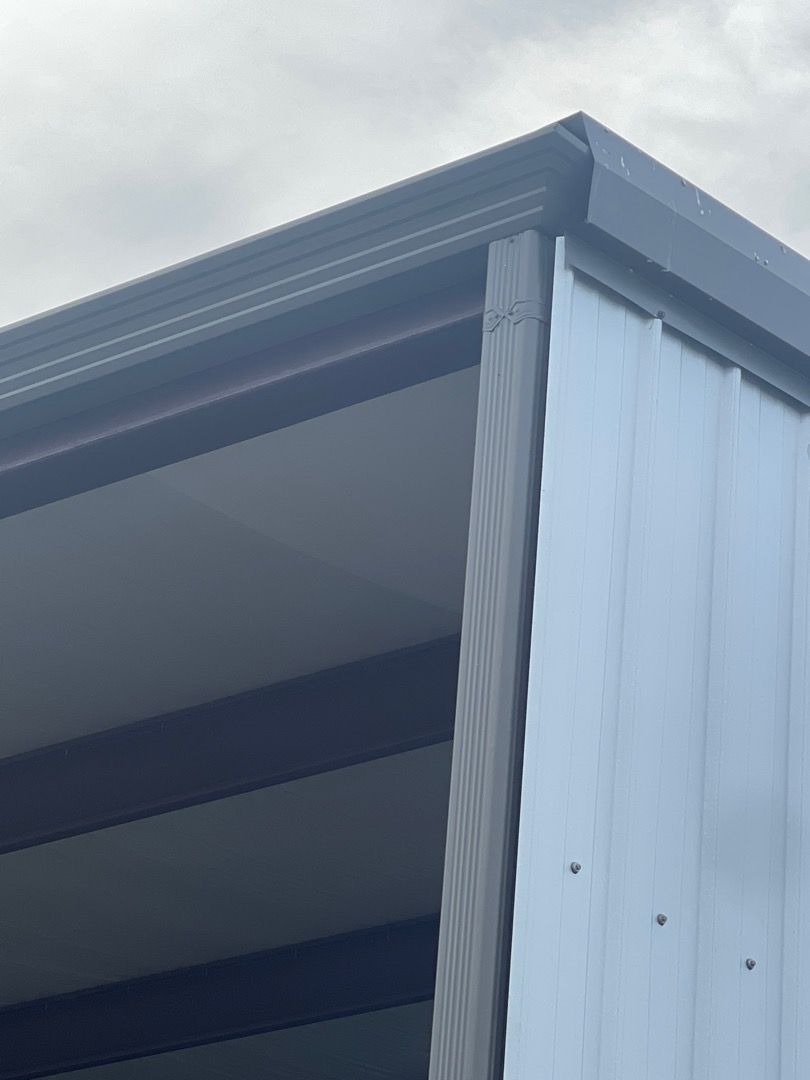 Gray metal building corner with dark trim and overcast sky.