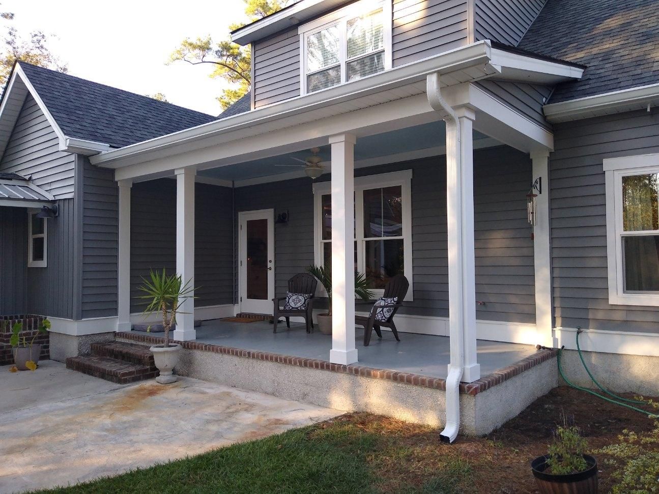 Gray house with white columns supporting a porch roof, two chairs visible.