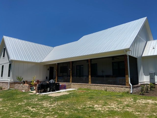 White farmhouse with a screened porch and metal roof under a blue sky.