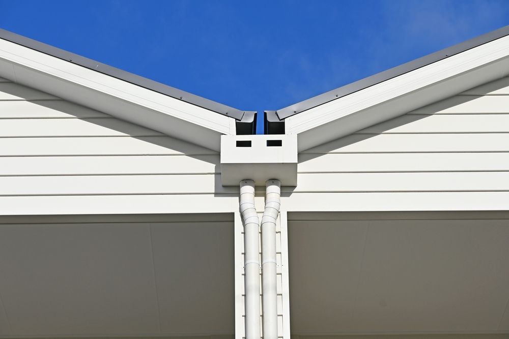 White house corner with rain gutters, against a clear blue sky.