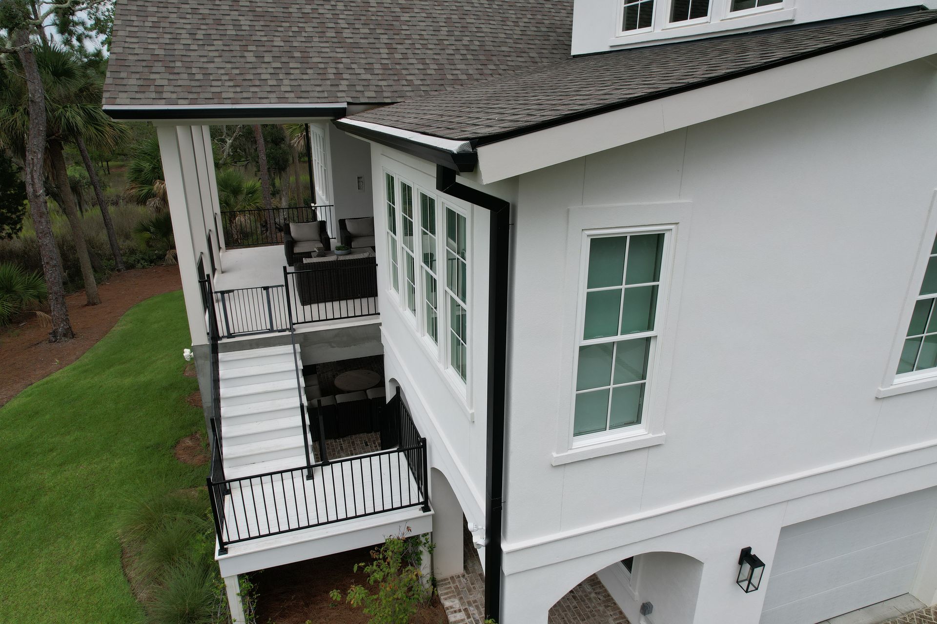 White house with multiple levels, balconies, and black railings, surrounded by green grass.