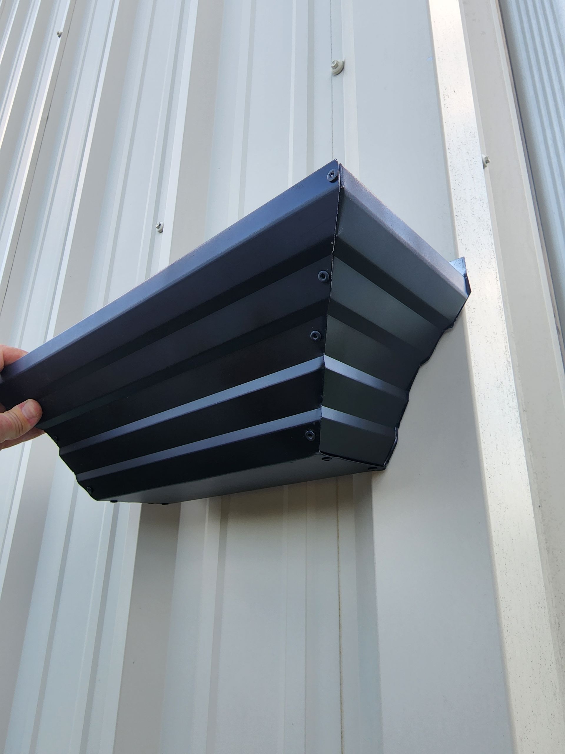 Dark blue metal gutter mounted on a white corrugated metal wall.