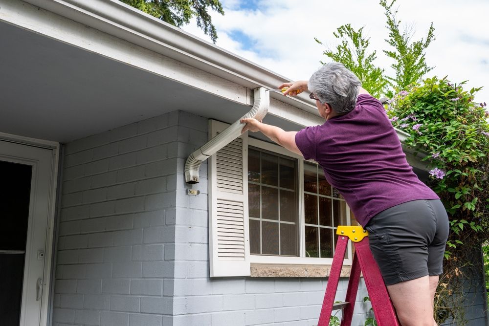Person on a ladder cleaning a gutter on a house.