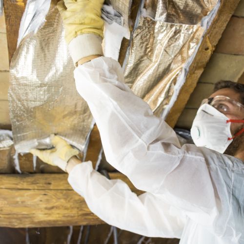 A man wearing a mask and gloves is holding a piece of insulation.