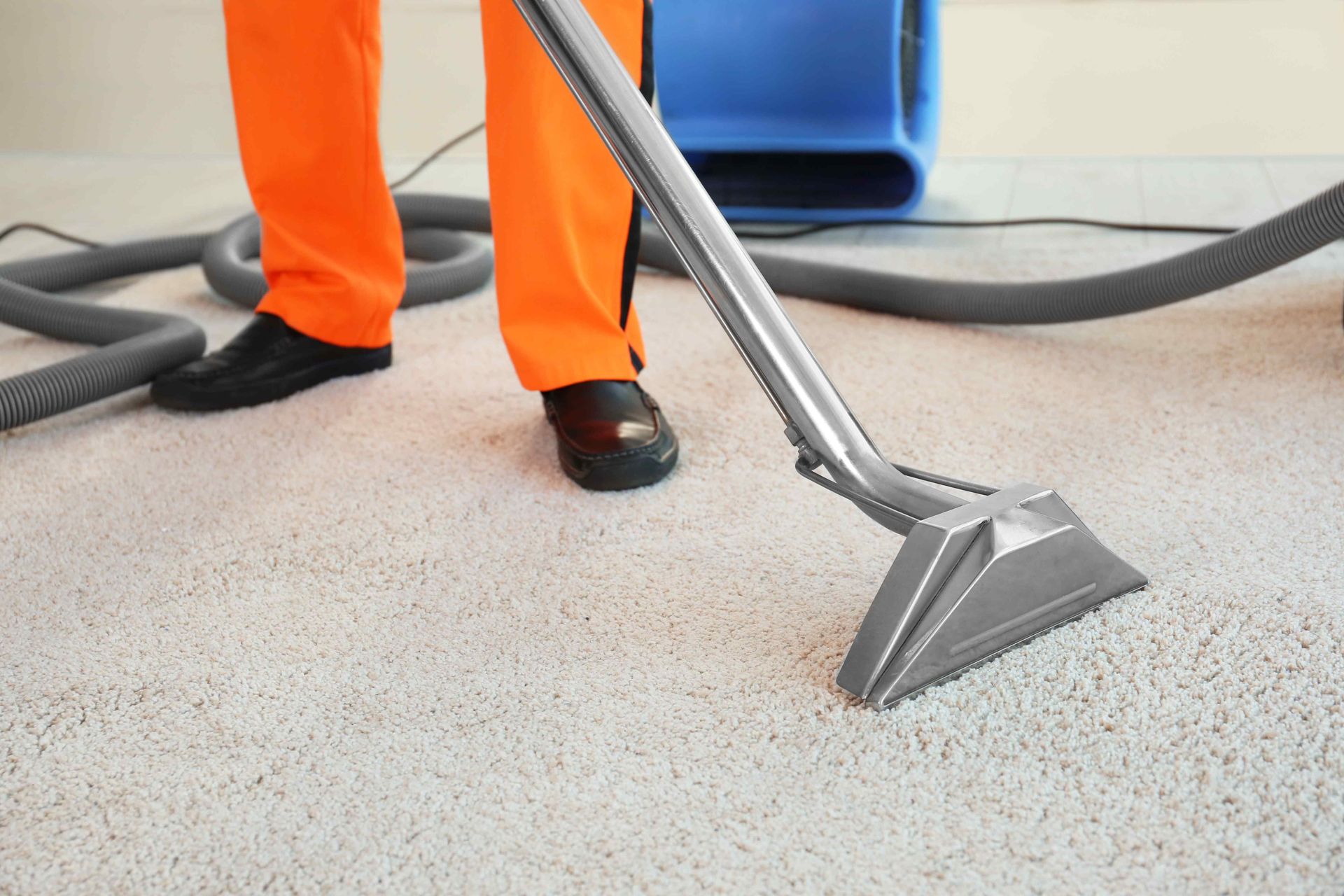 An employee wearing orange while cleaning a carpet floor