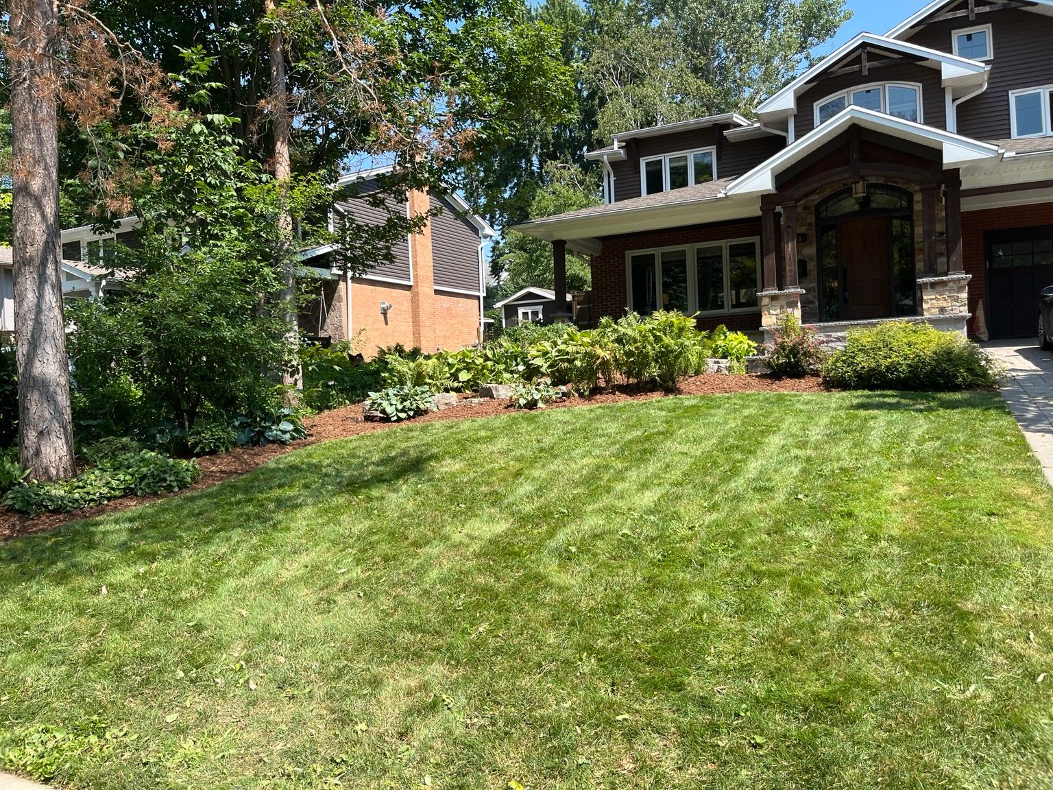 Front yard with green lawn, trees, and a house with a porch and stone chimney