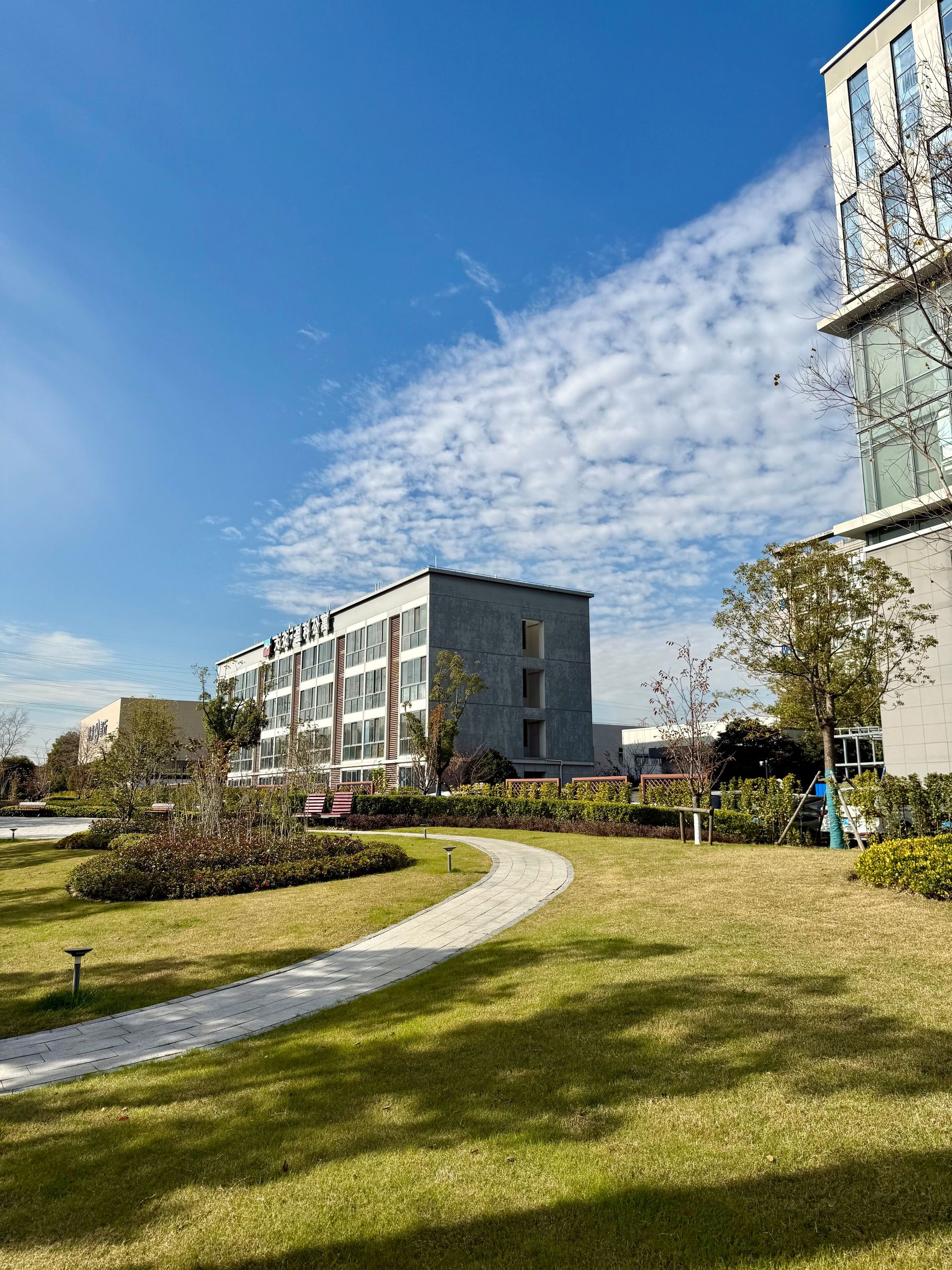 Modern apartment buildings beside a curved walkway and green lawn under a bright blue sky