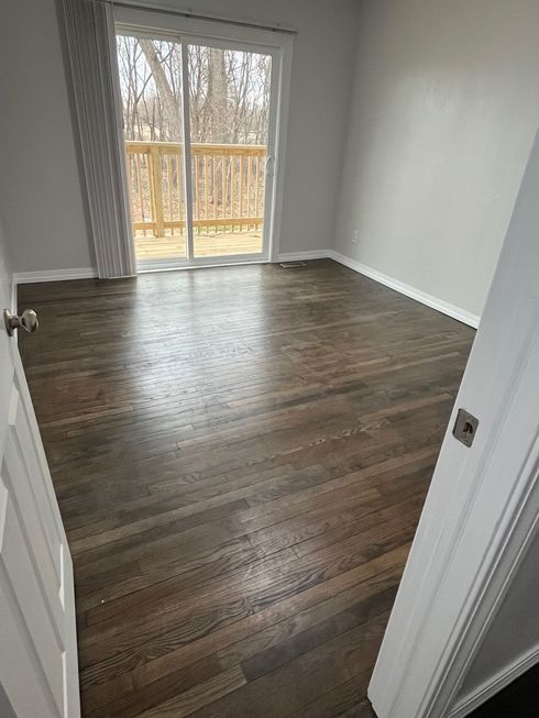 Empty room with dark hardwood floors, grey walls, and a sliding glass door leading to a wooden deck.