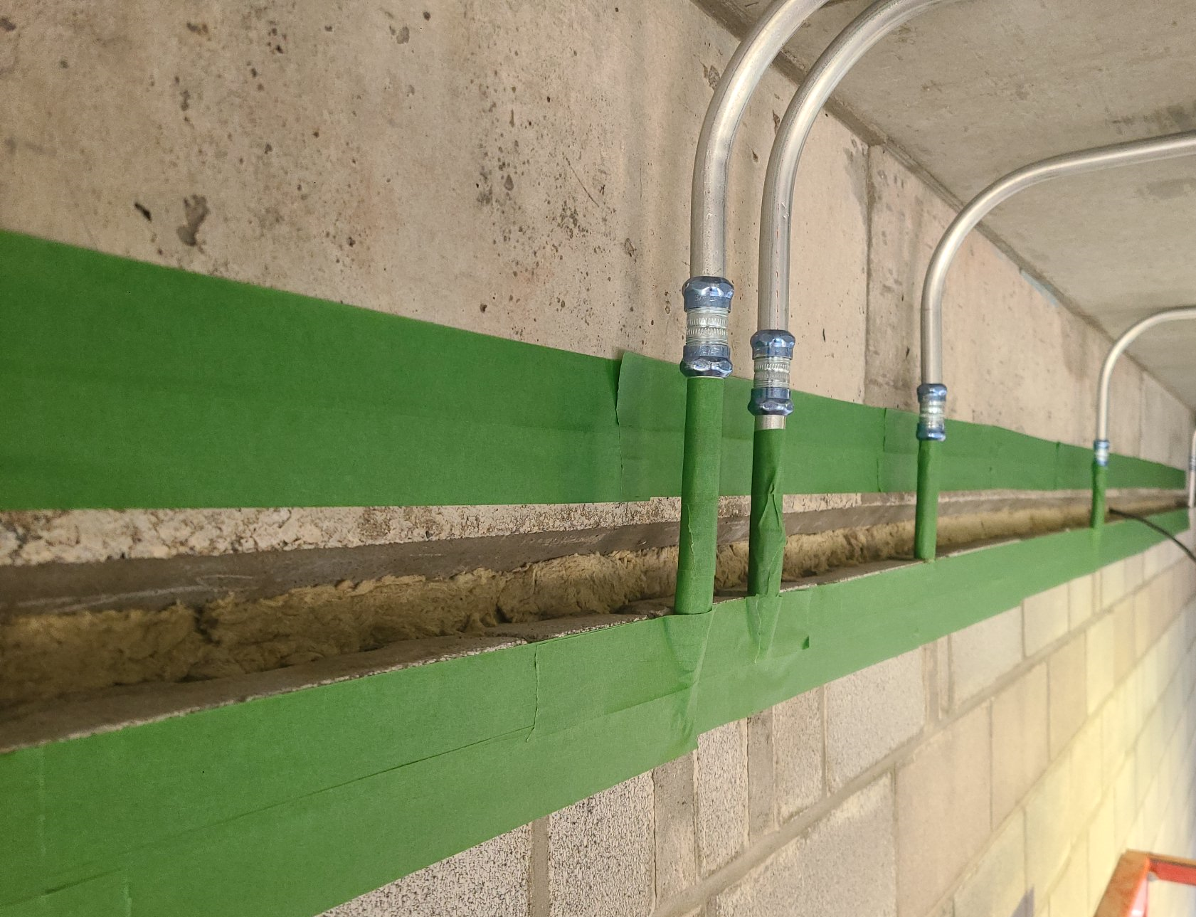 Une rangée de tuyaux verts est reliée à un mur de briques.