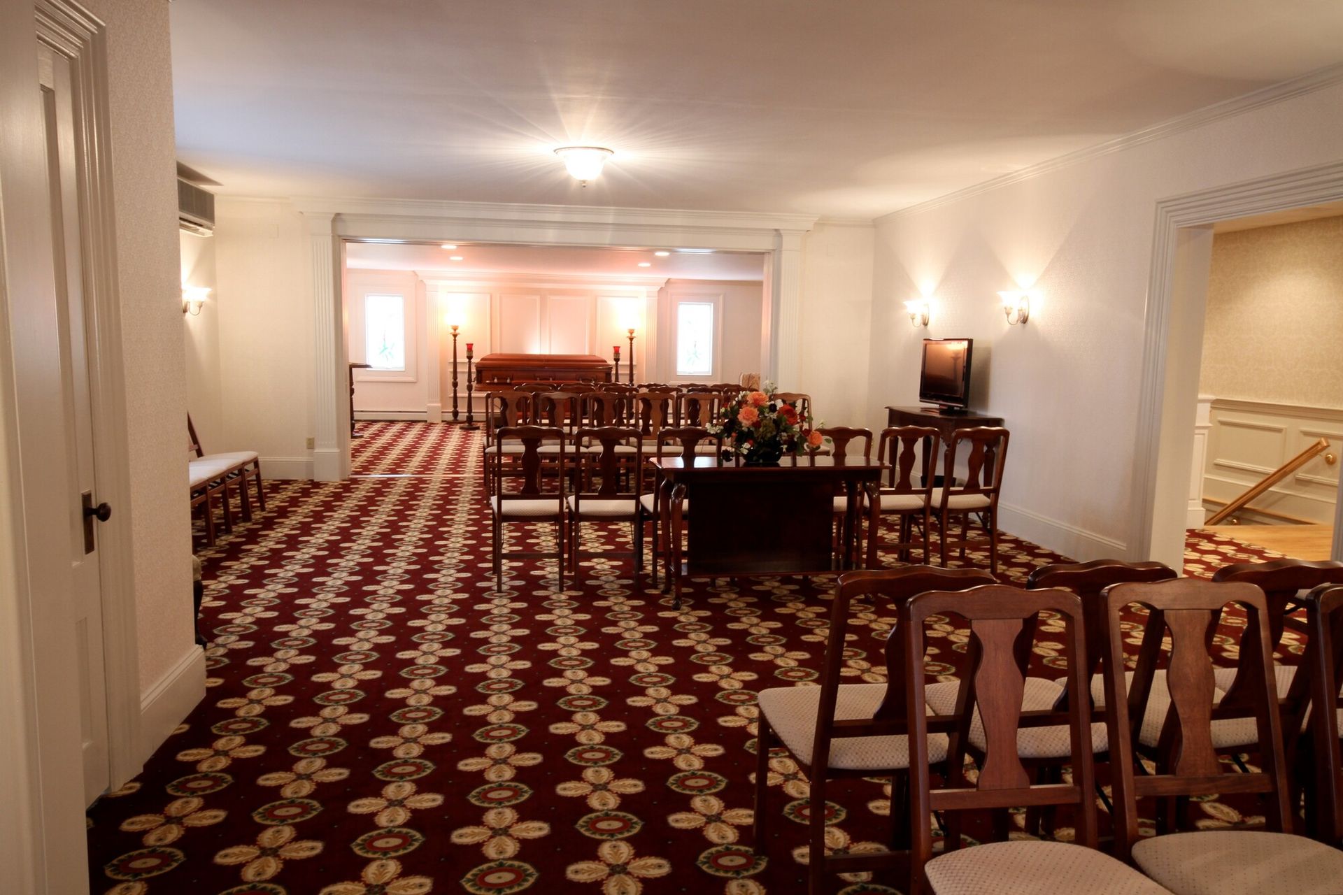 Elegant hotel dining room with red patterned carpet, wooden tables, and warm wall sconces