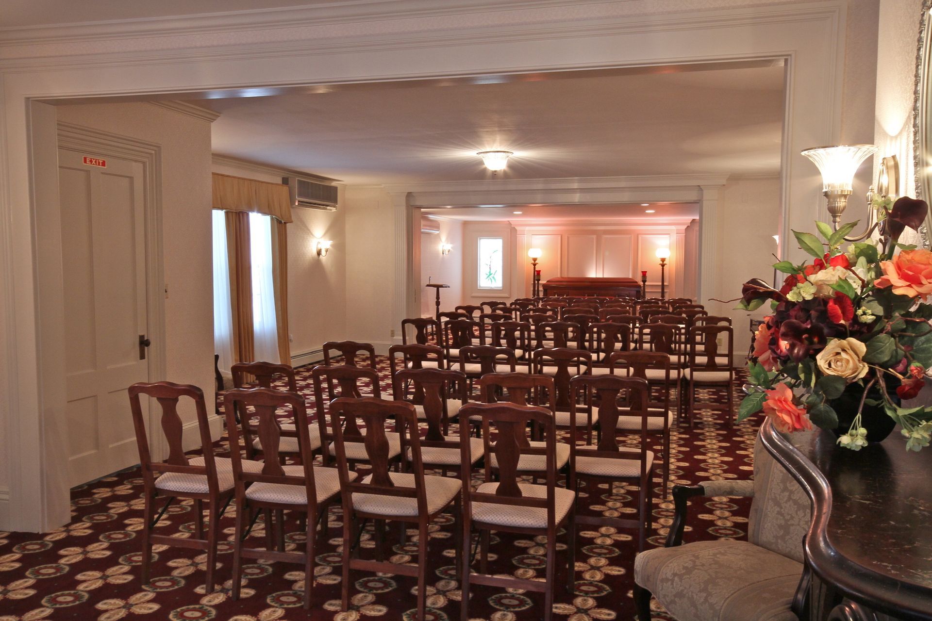 Empty banquet hall with rows of chairs, patterned carpet, and floral arrangement on a side table