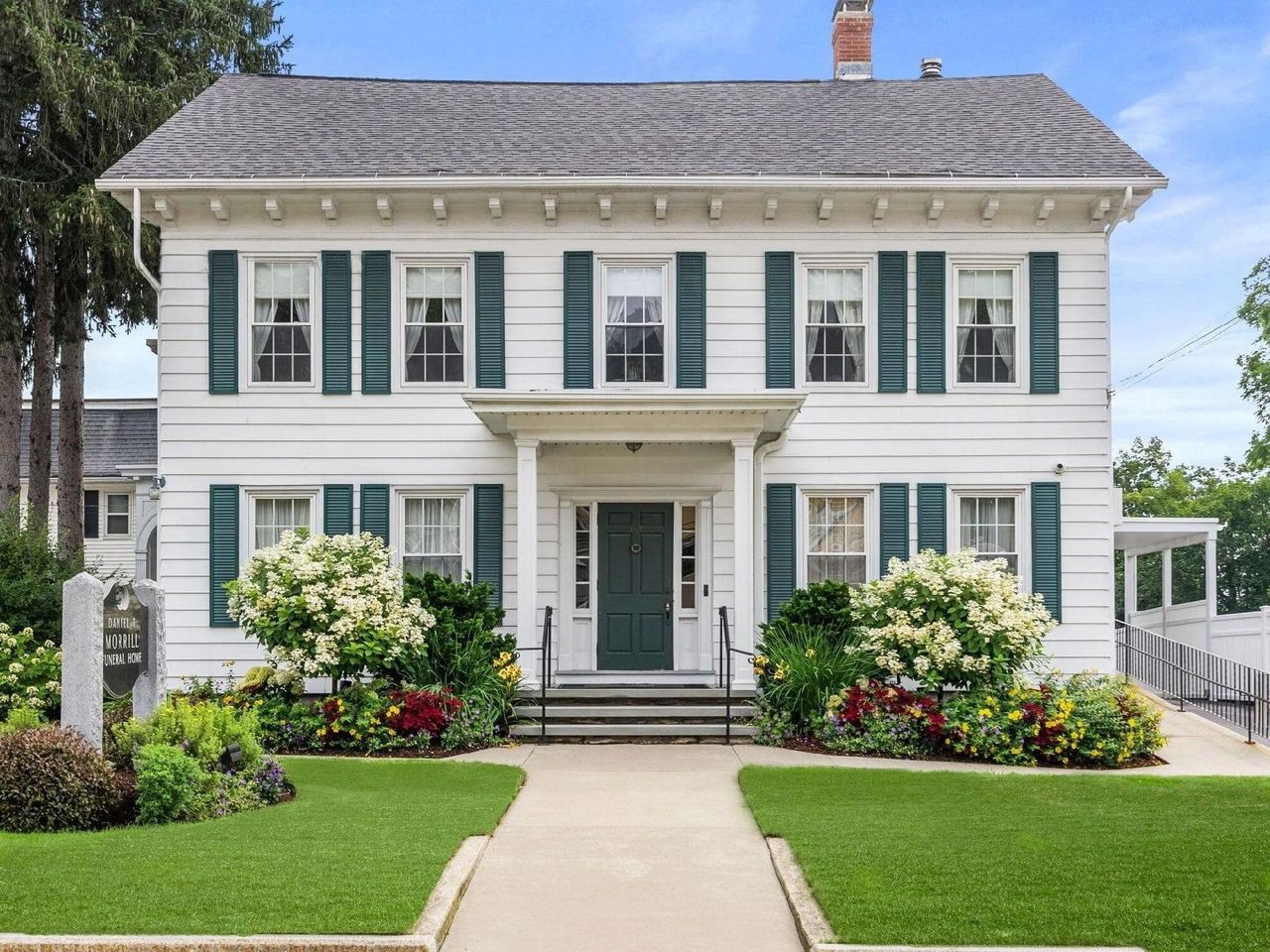 White two-story house with green shutters, front porch, and manicured lawn.