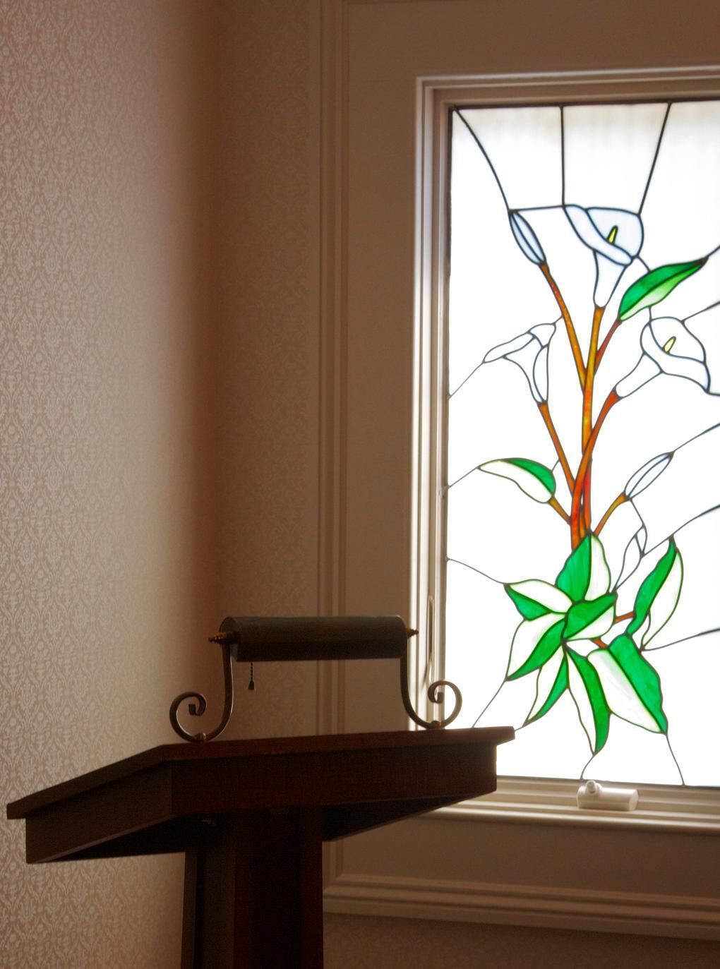 Stained glass window with green leaves and orange branches above a dark wooden mantel