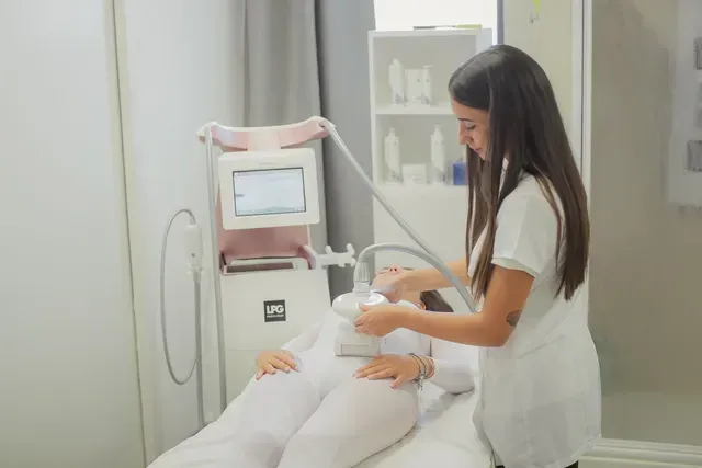 In una luminosa stanza di una clinica, una donna in uniforme bianca utilizza un dispositivo per il viso su un paziente.