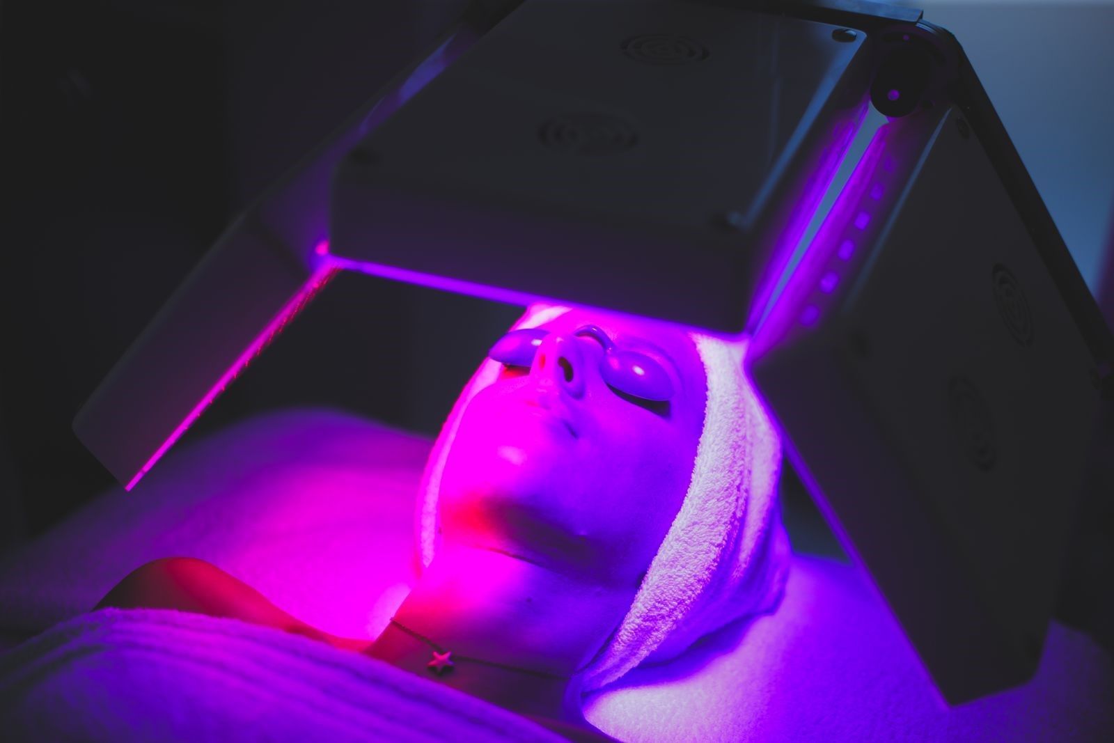 Persona sdraiata sotto un oggetto scuro, illuminato da una vivida luce al neon viola.
