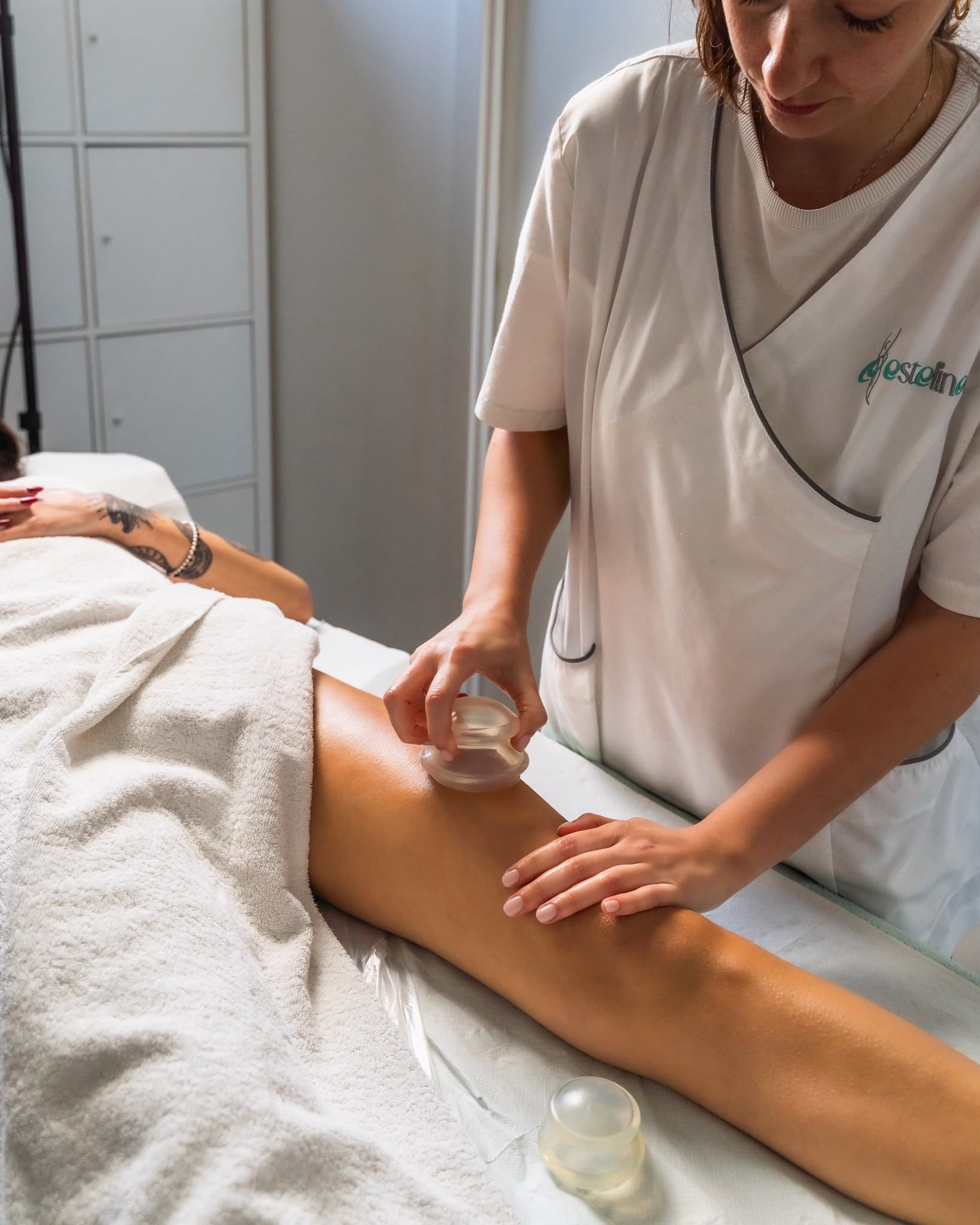 In un centro benessere, una persona applica una lozione sulla gamba di un'altra persona utilizzando un dischetto di cotone.