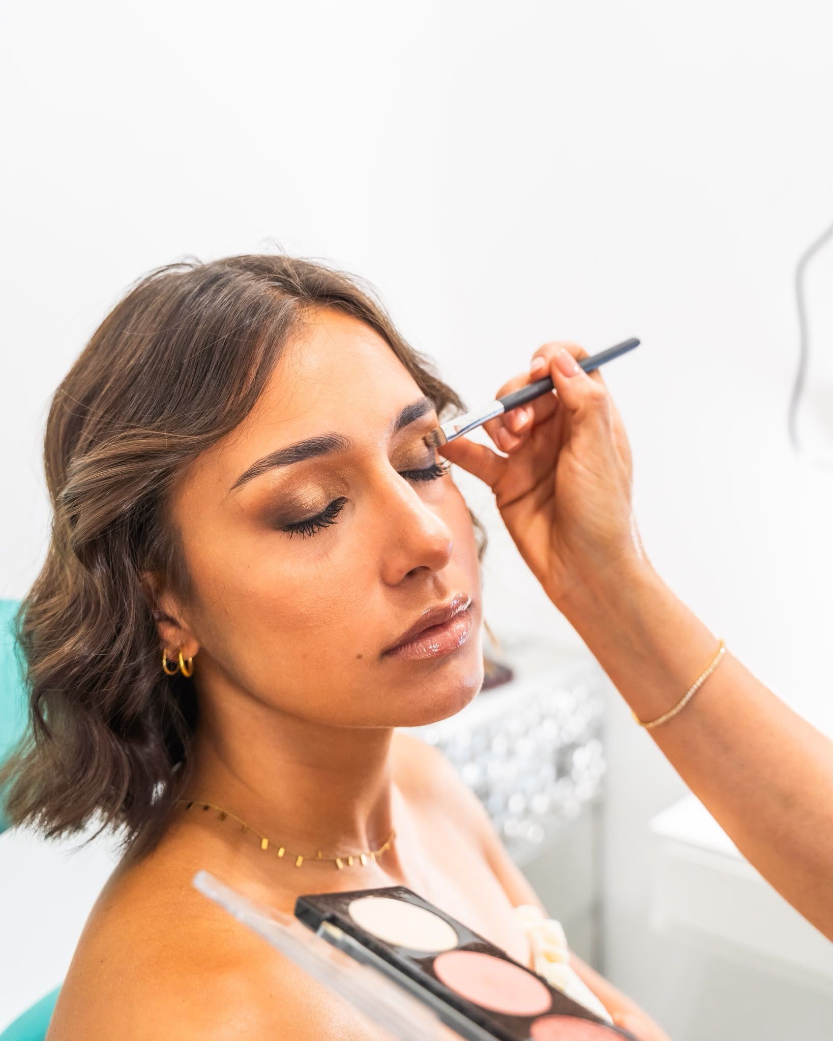 Truccatrice che applica il trucco occhi a una donna che tiene in mano una tavolozza e un pennello.