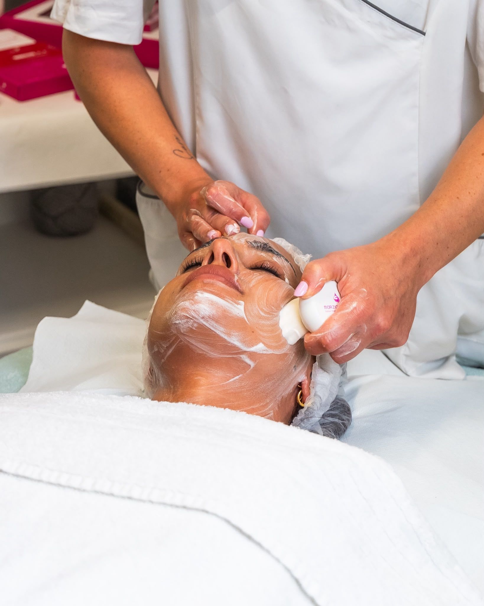 Persona che riceve un trattamento viso mentre le viene applicata una crema e le mani massaggiano il viso in un ambiente spa.