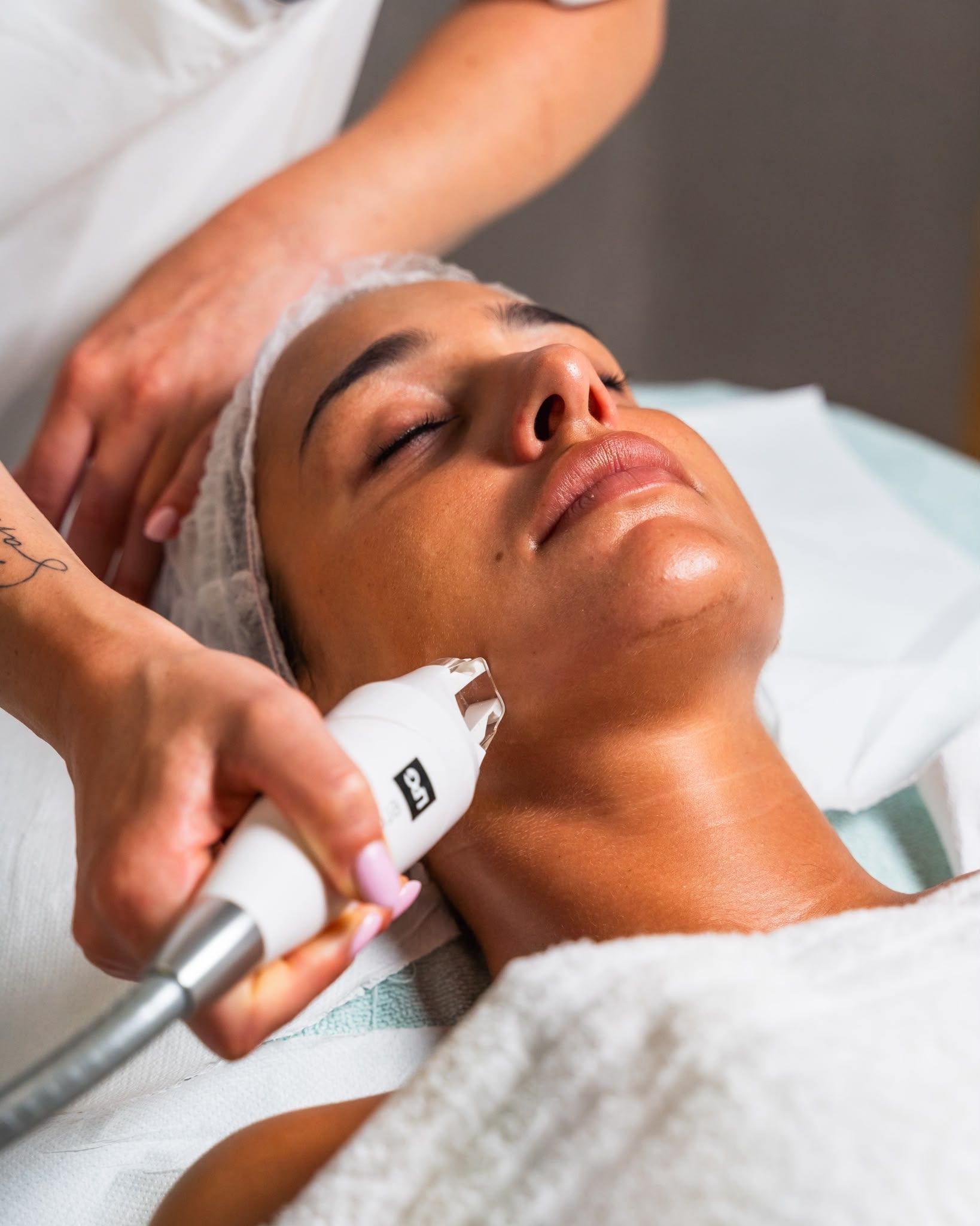 Trattamento viso con dispositivo portatile applicato sulla guancia di una donna in un ambiente spa.
