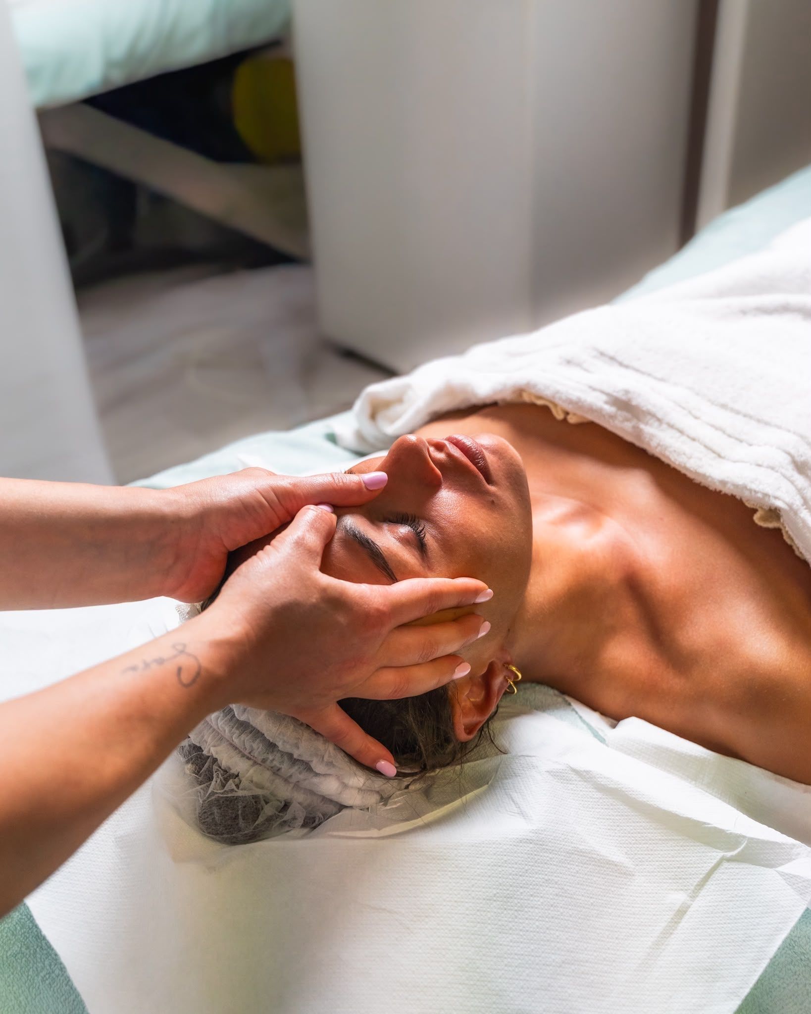 Una persona riceve un massaggio al viso mentre è sdraiata su un lettino da spa, coperta da un asciugamano.