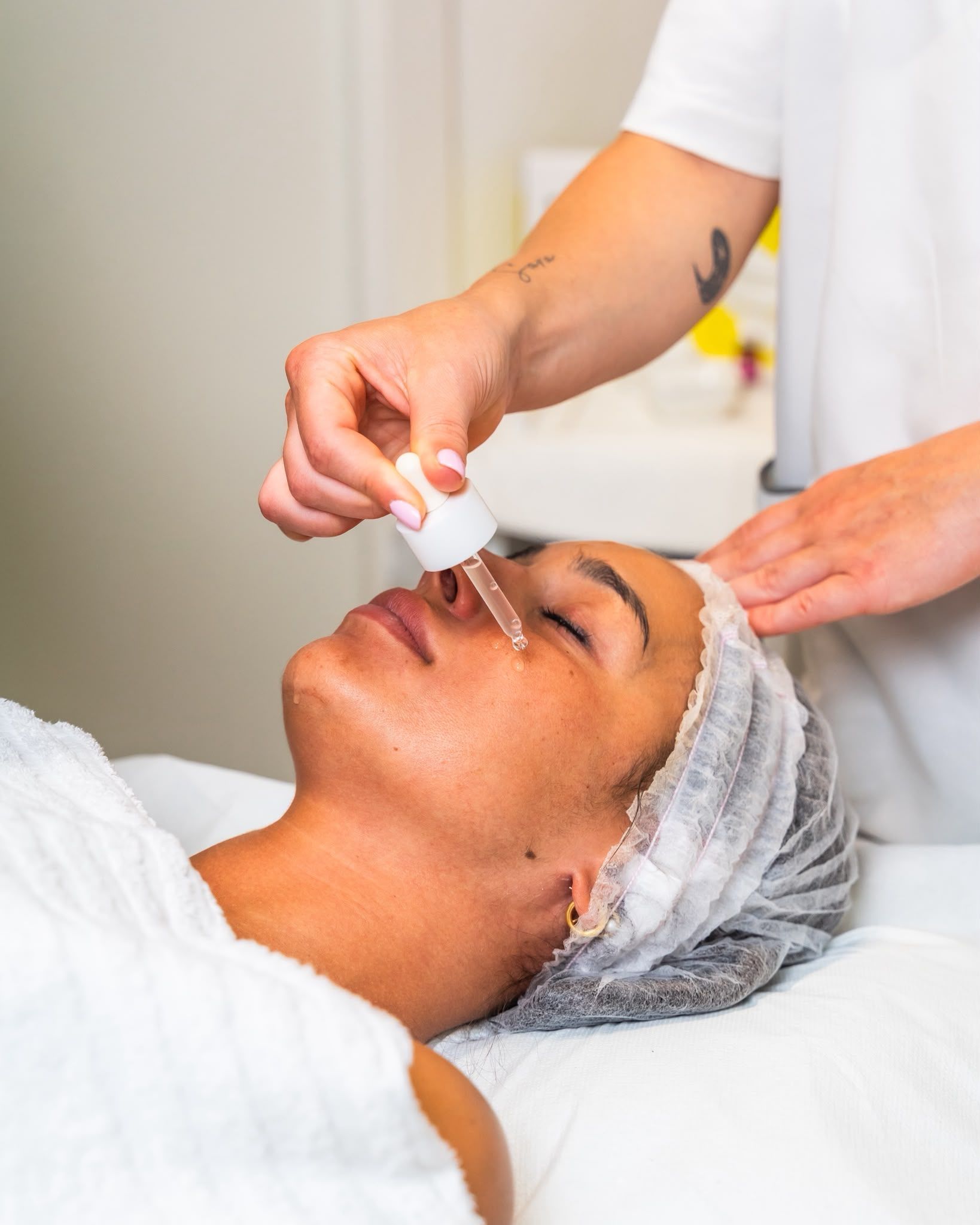 Trattamento viso in spa, siero applicato su una cliente che indossa un asciugamano bianco e una cuffia per capelli.