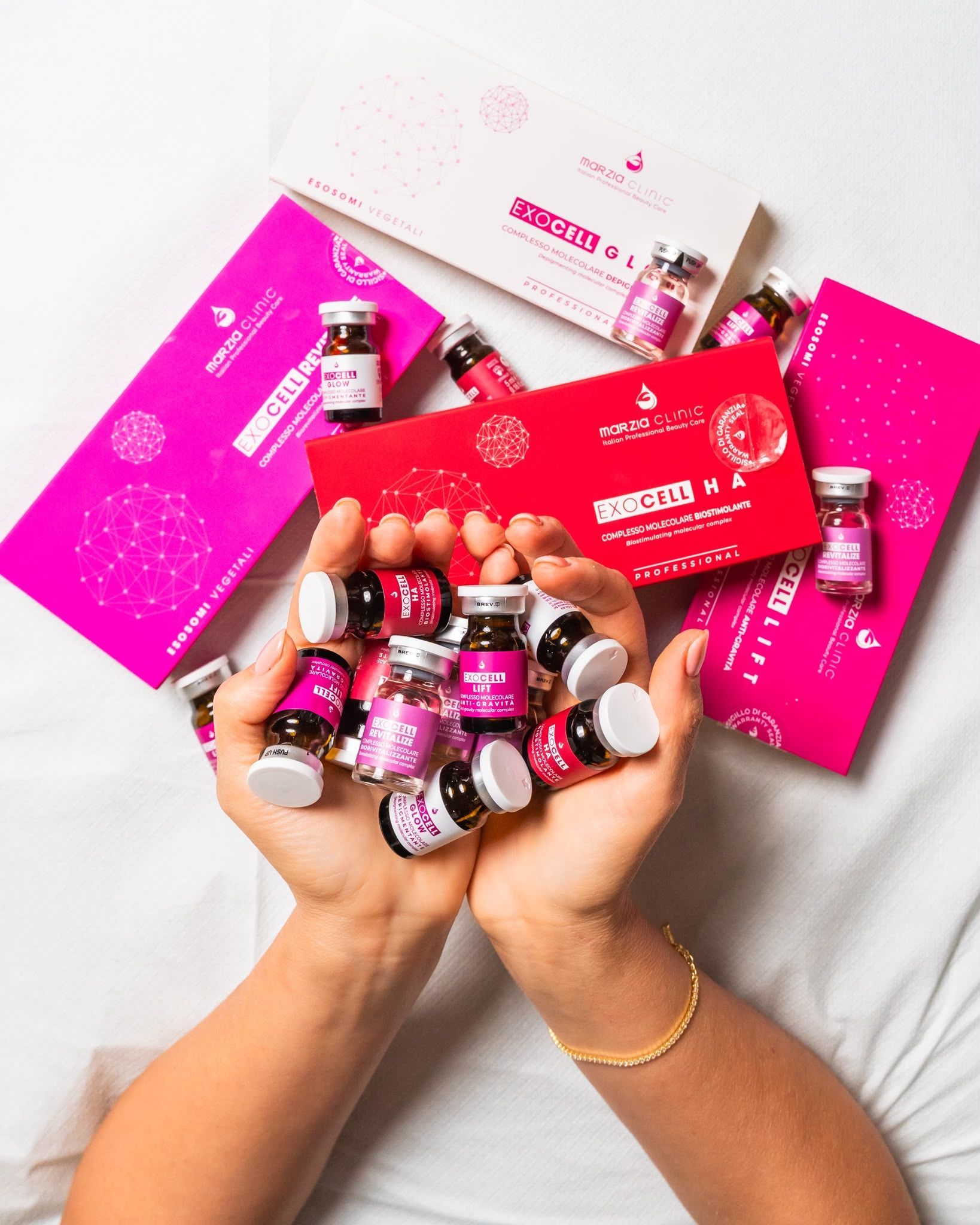 Mani che reggono prodotti cosmetici rosa e scatole su una coperta bianca