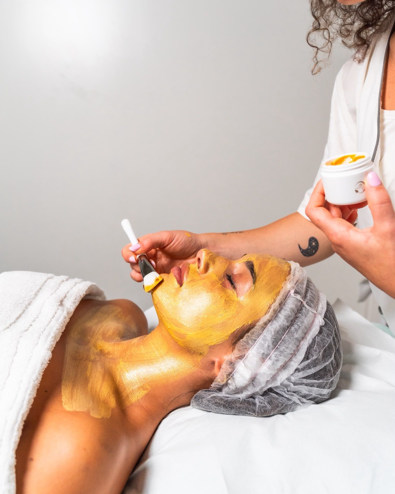 Una persona applica una maschera viso all'oro a un cliente sdraiato su un lettino da spa.