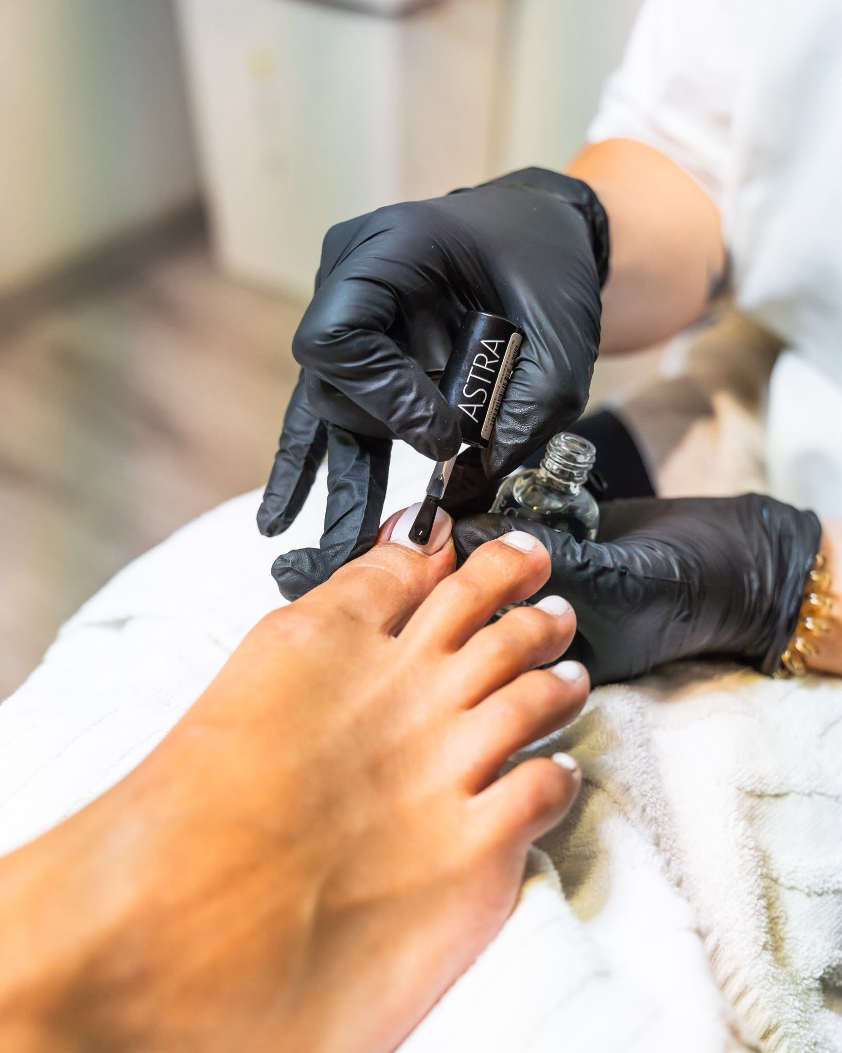 Mani guantate di nero applicano lo smalto sulle unghie dei piedi di una persona durante una pedicure.