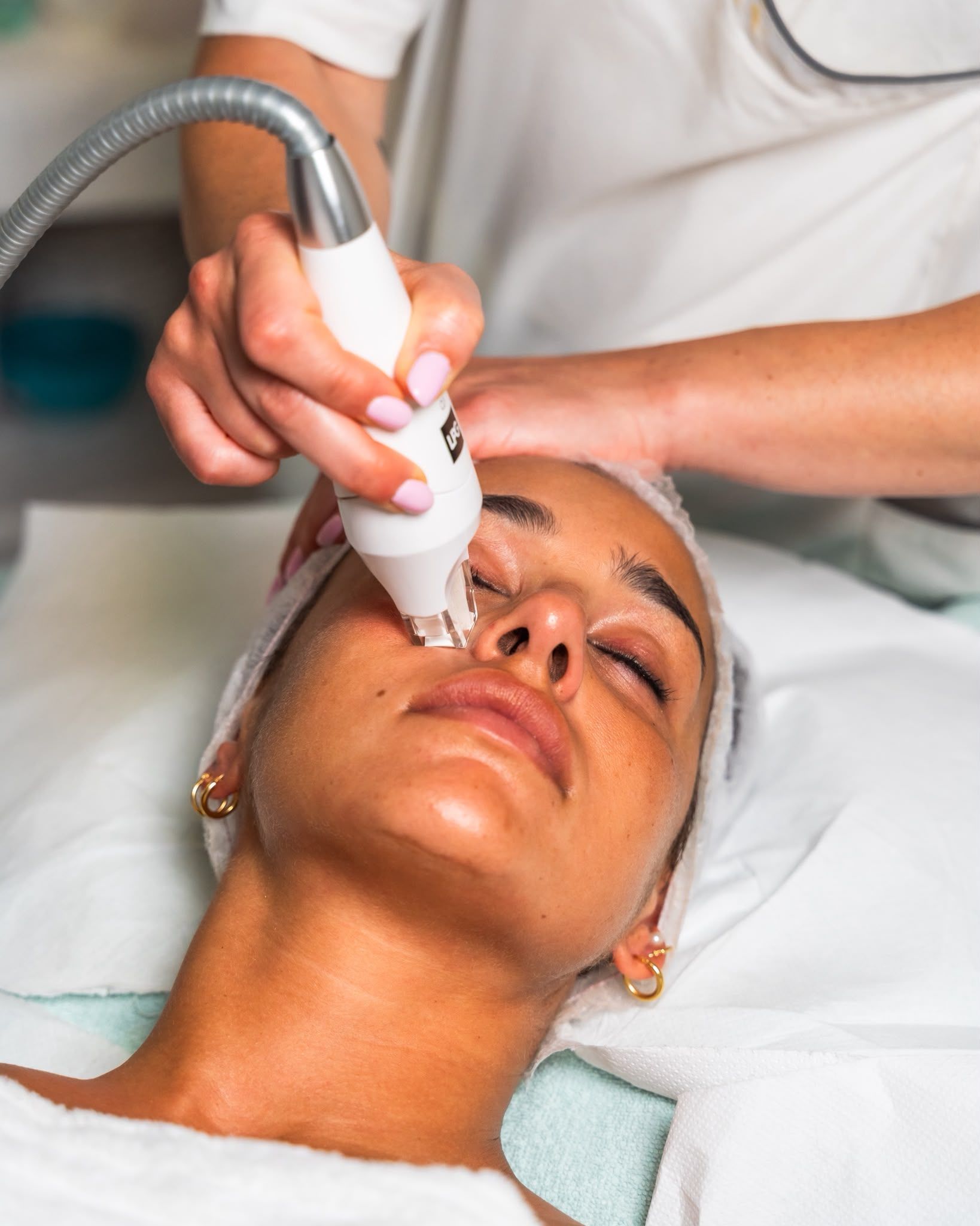 Trattamento viso con dispositivo portatile su cliente sdraiato in un ambiente spa.