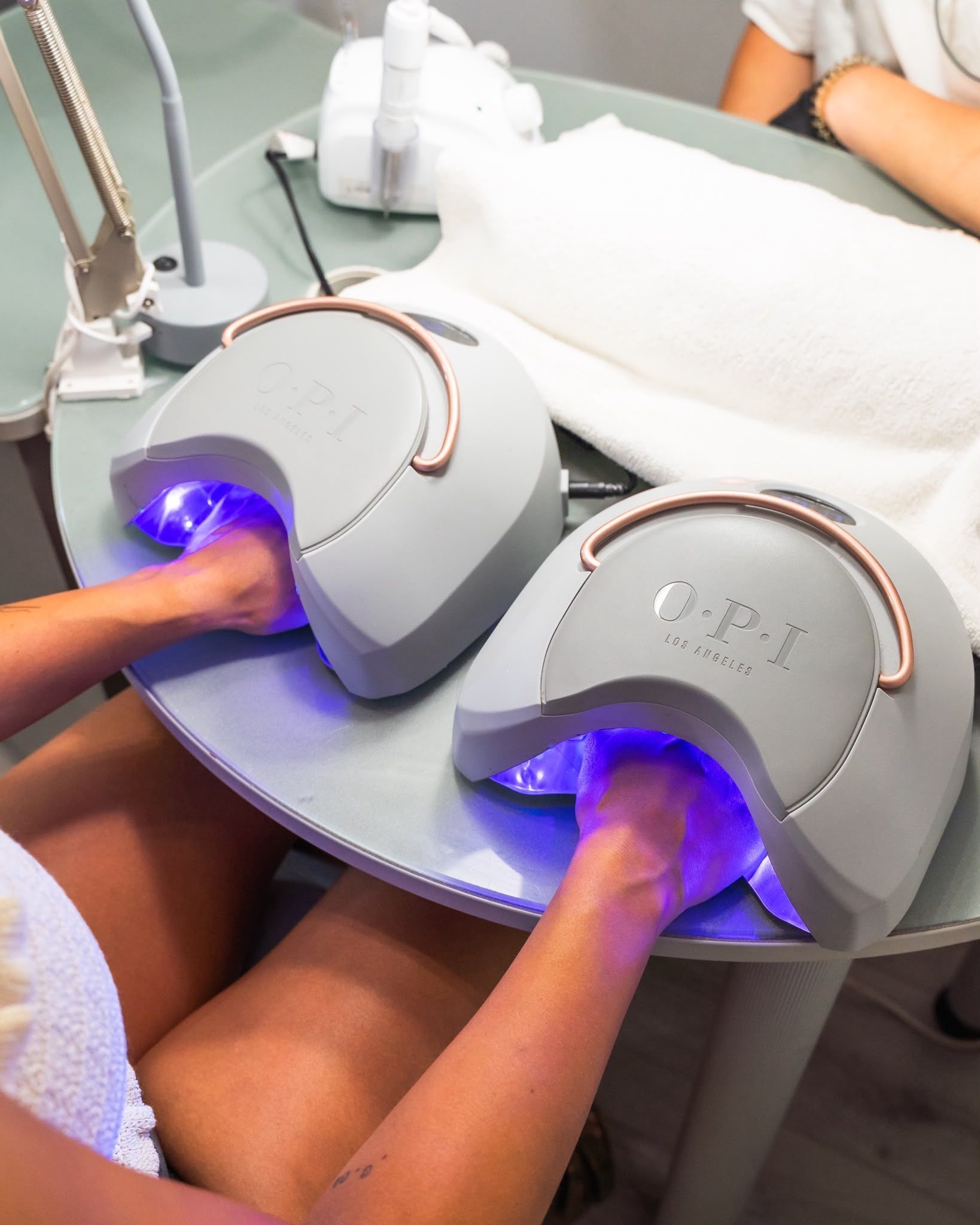 Mani immerse in lampade UV a luce blu su un tavolo per manicure.