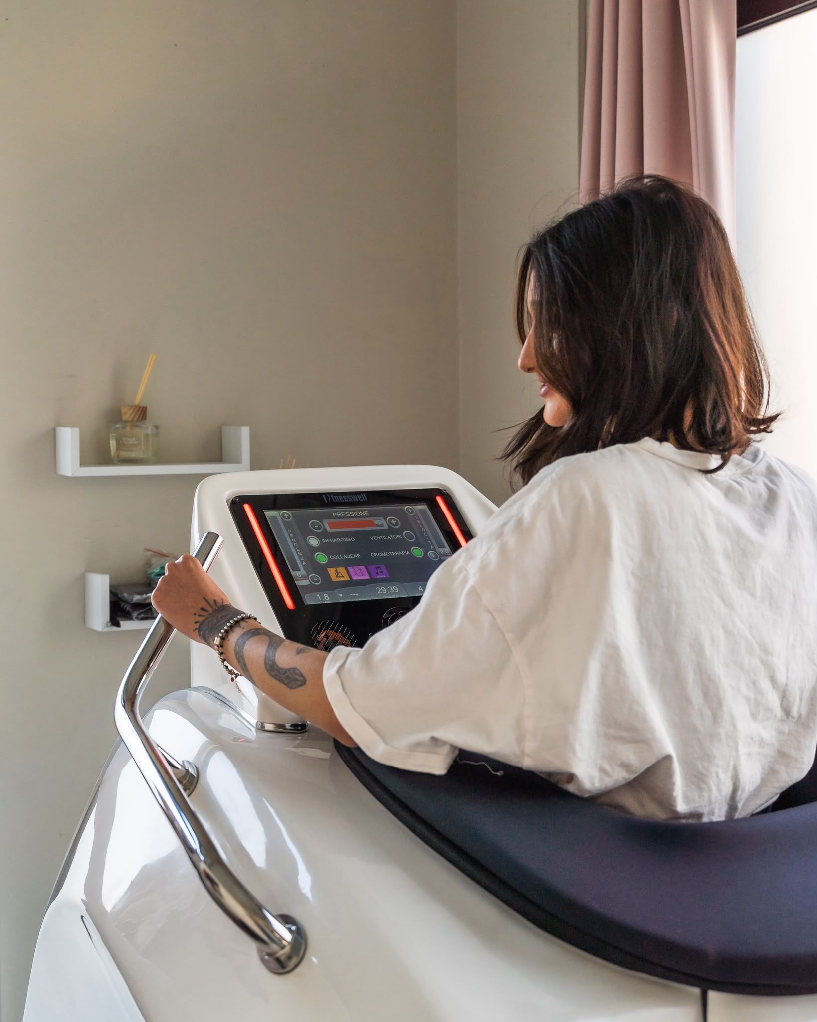 Una persona seduta su una poltrona massaggiante utilizza un tablet in una stanza illuminata da una luce soffusa.