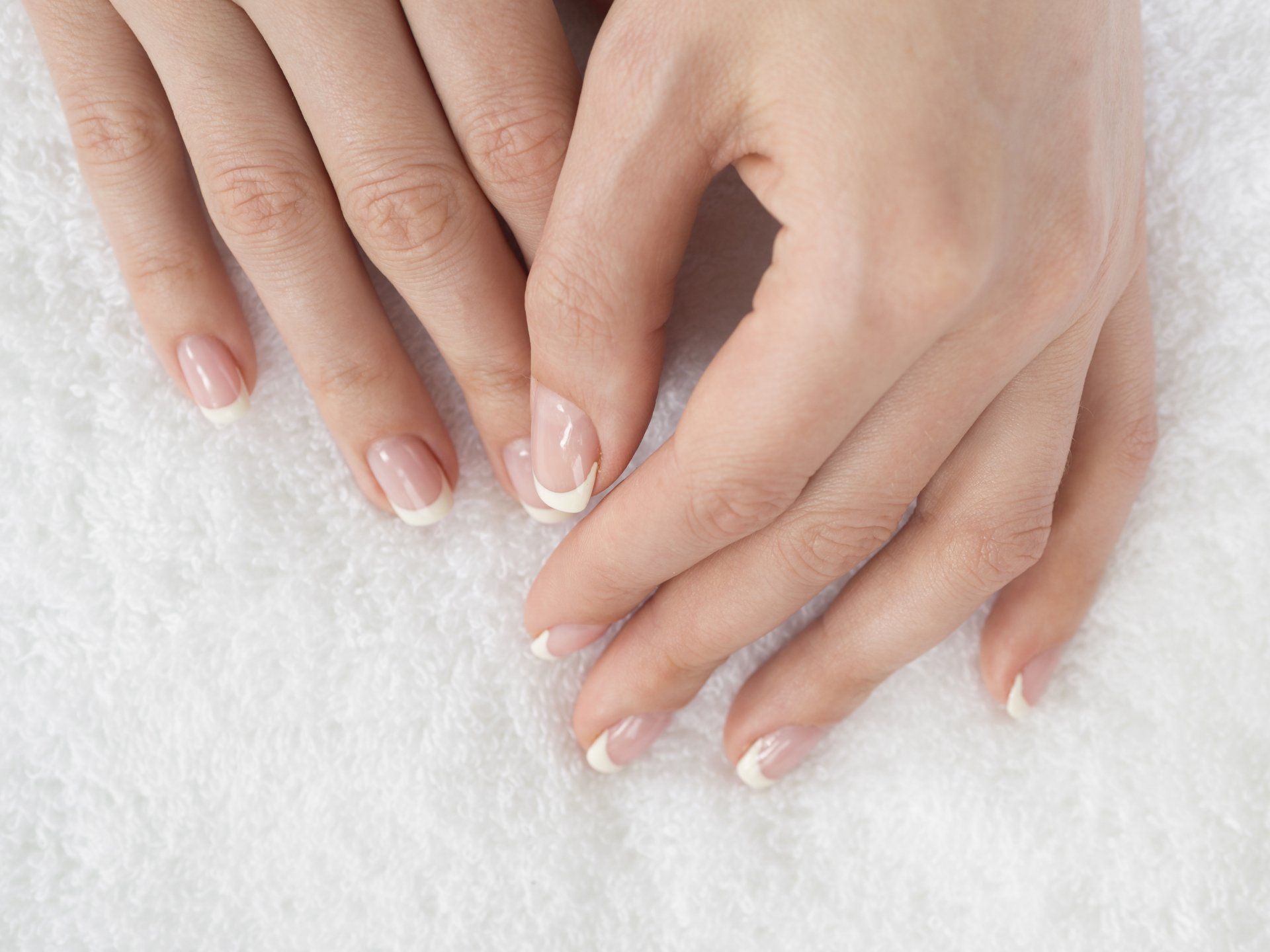Mani con unghie curate di un rosa pallido appoggiate su un asciugamano bianco dalla consistenza ruvida.