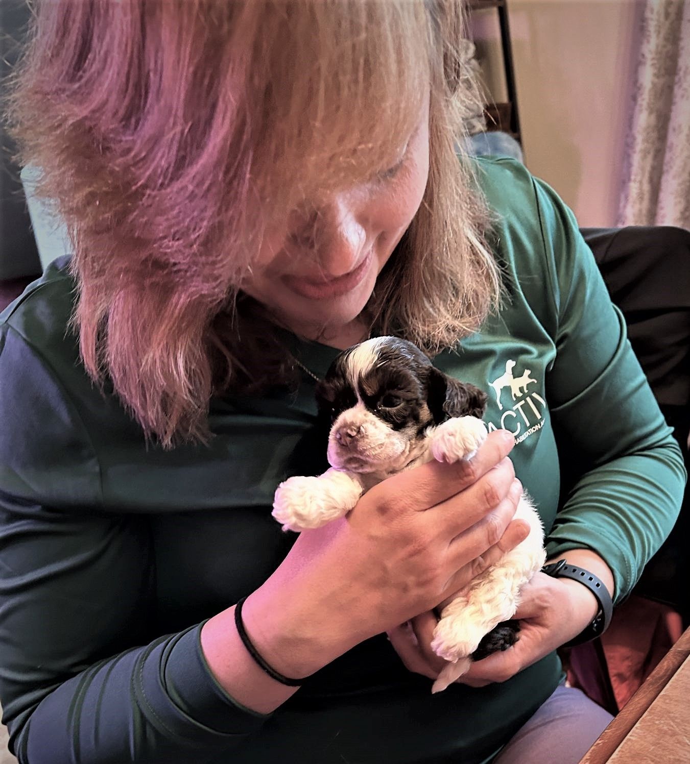 Woman holding a tiny black-and-white puppy close to her chest indoors