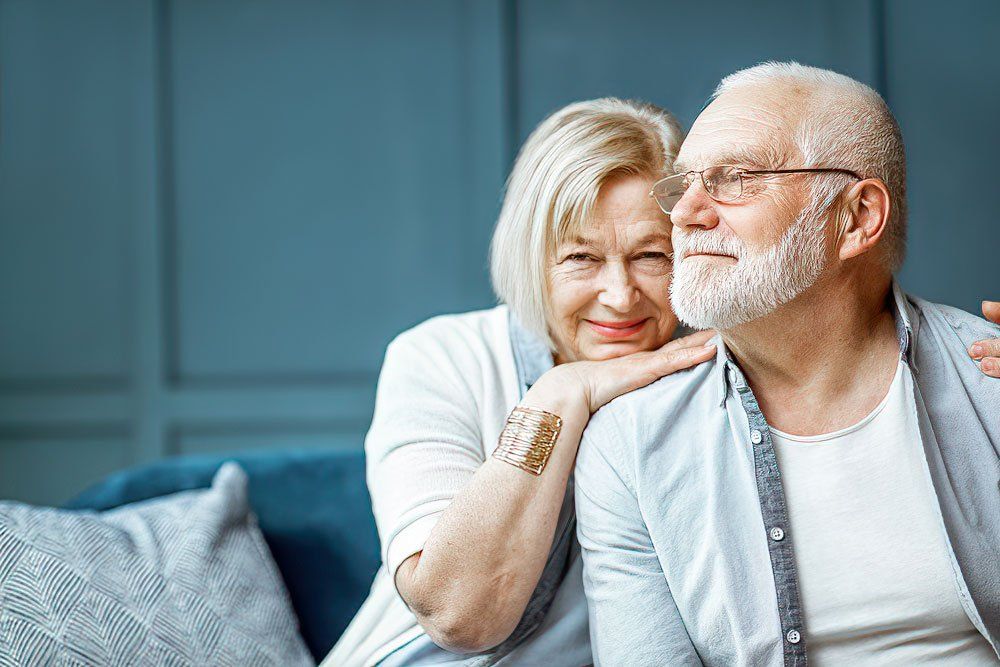 An elderly couple is sitting on a couch and hugging each other.