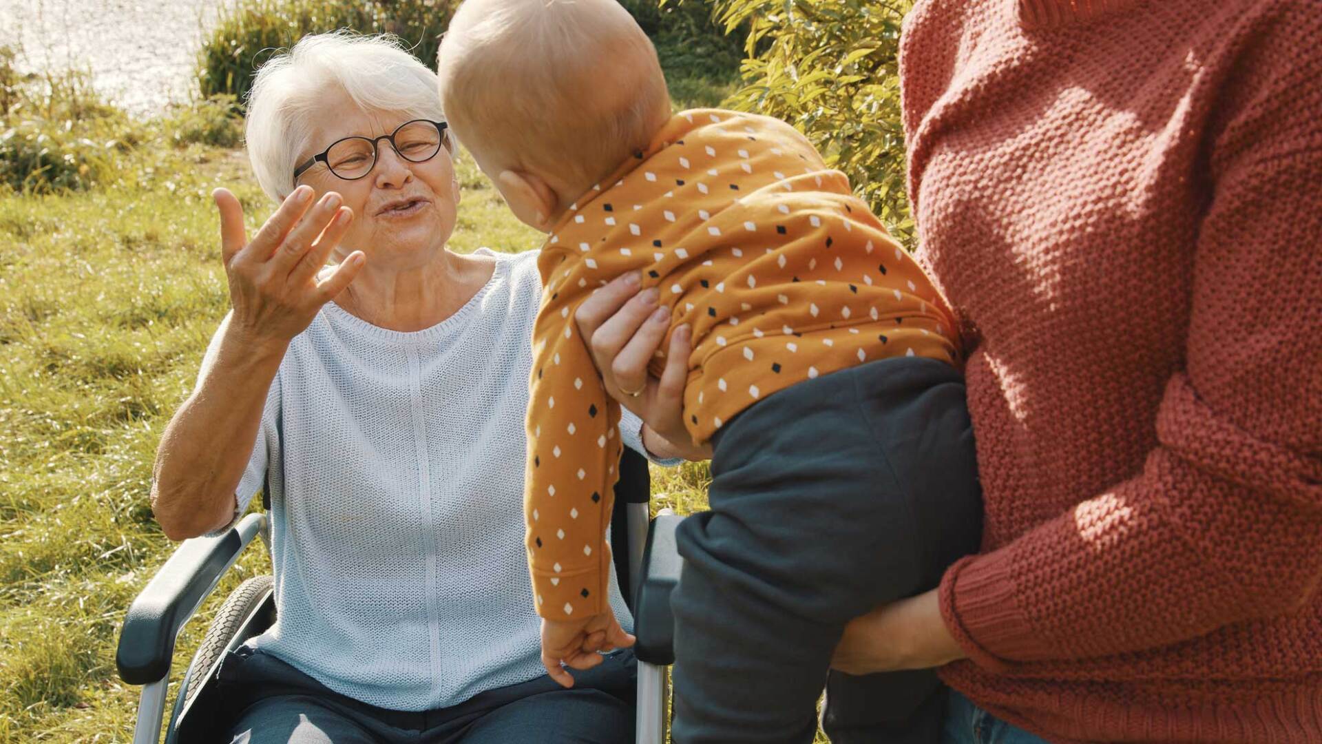 An elderly woman in a wheelchair is holding a baby.