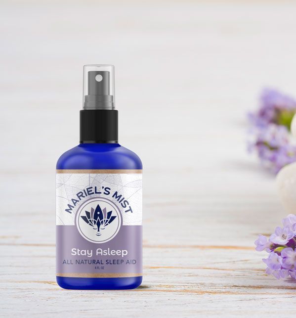 A bottle of mariel 's mist is sitting on a wooden table next to purple flowers.