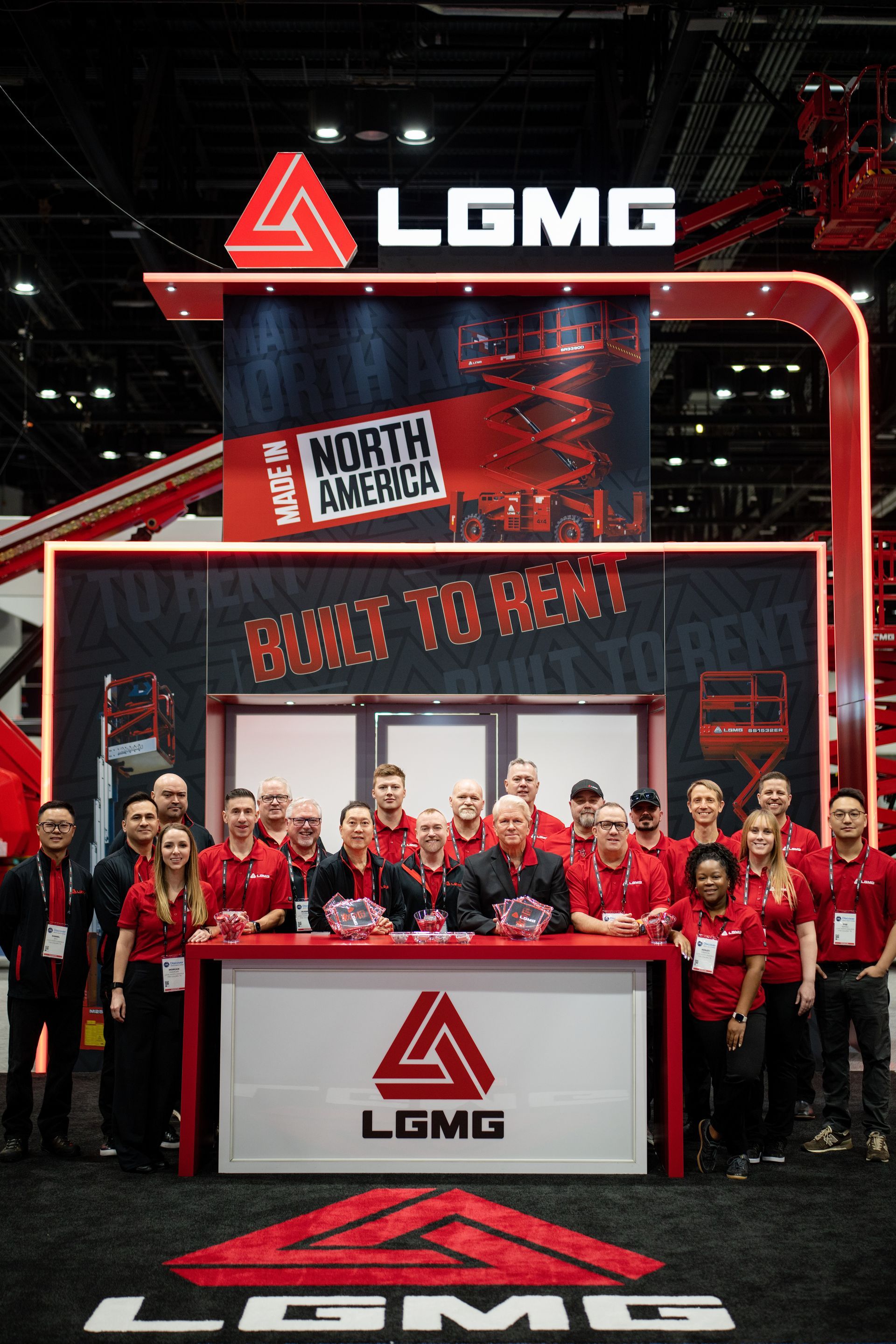 LGMG booth with a group posing in red shirts at a trade show, under bright red signage and lights