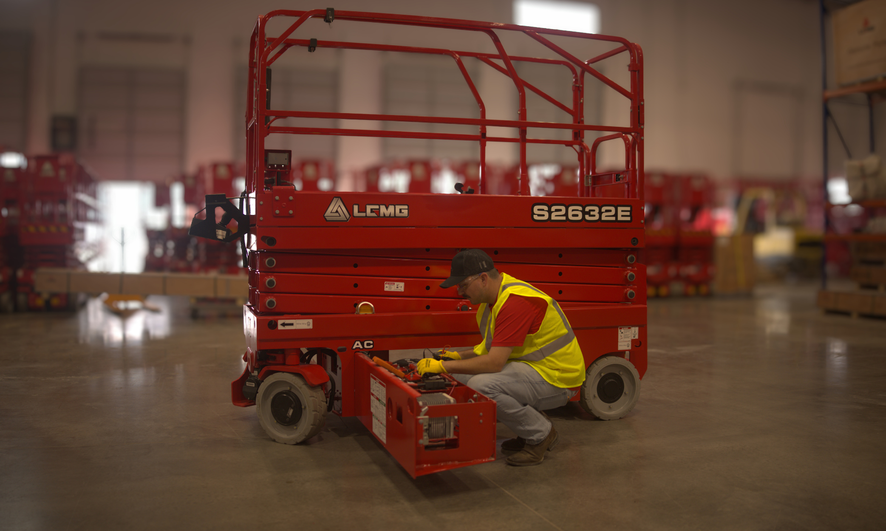 Scissor Lift inside a warehouse with technician working on the battery compartment.